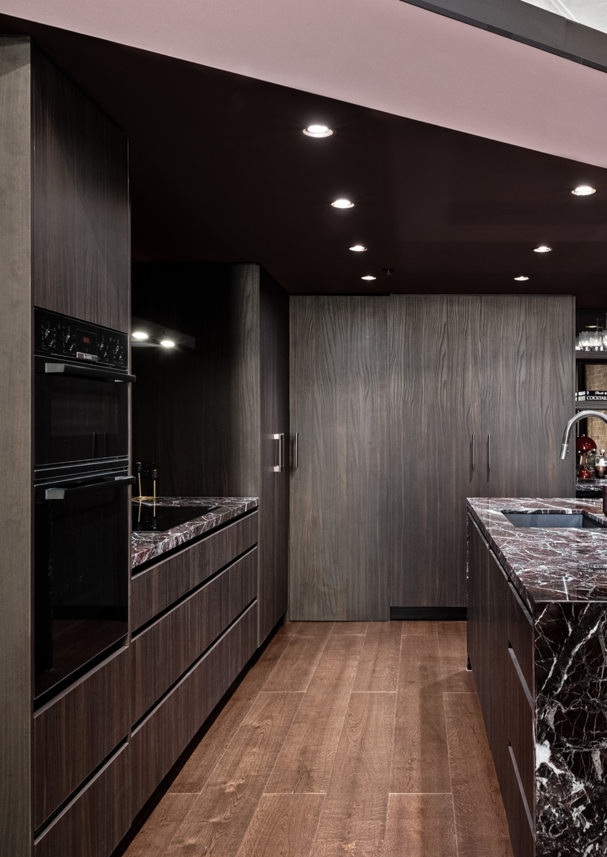 Modern kitchen with dark wood cabinets, marble countertops, and recessed ceiling lights.