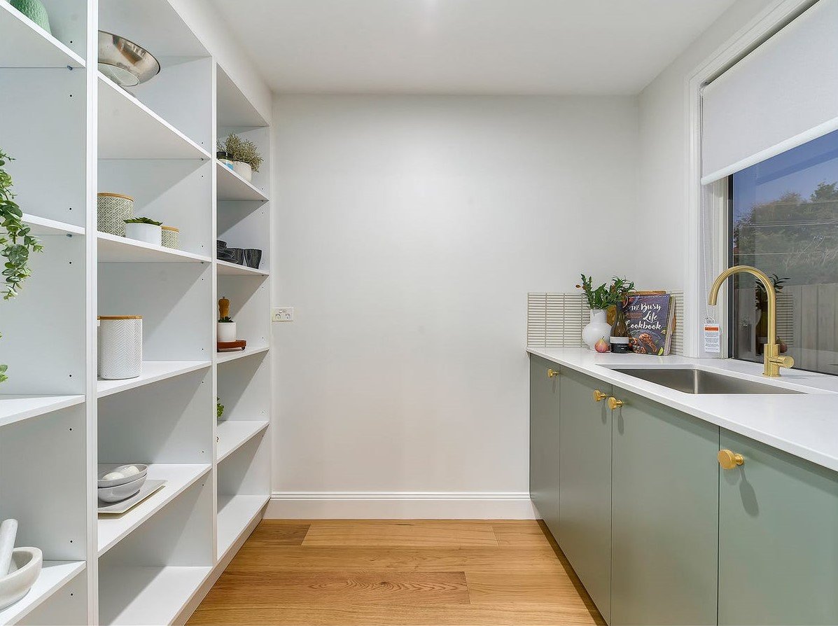 Modern kitchen with white shelves, green cabinets, a kitchen sink, a window, and decorative items like plants and books.