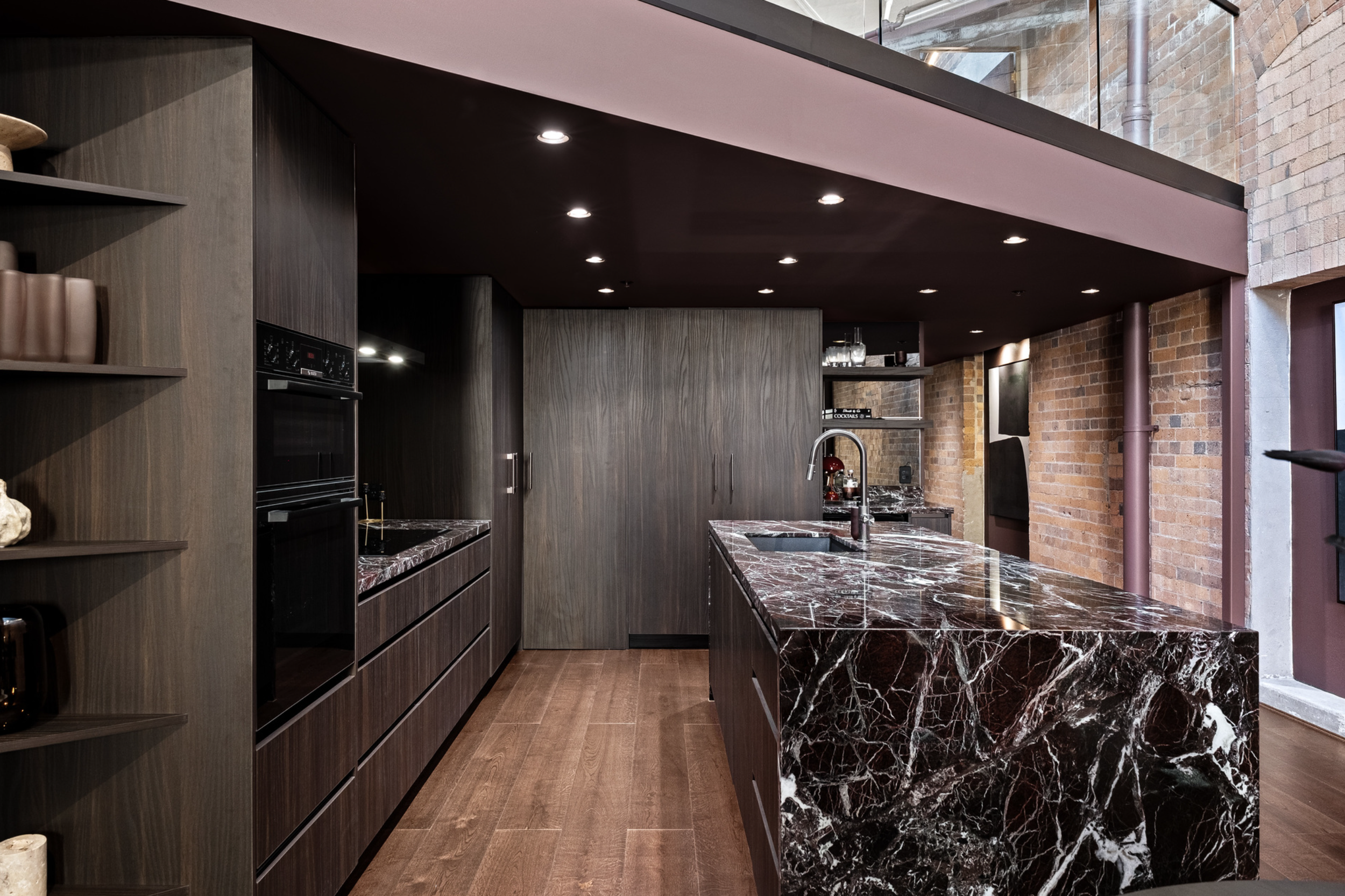 Modern kitchen with dark wood cabinetry, black and white marble countertops, brick wall, and industrial style windows.