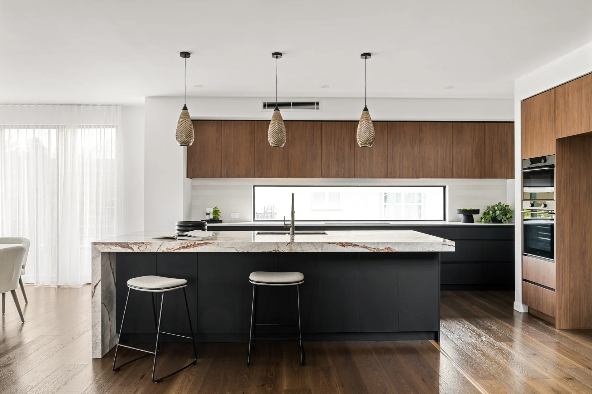 Modern kitchen with black and wood cabinetry, marble countertop island, pendant lights, and hardwood floors.