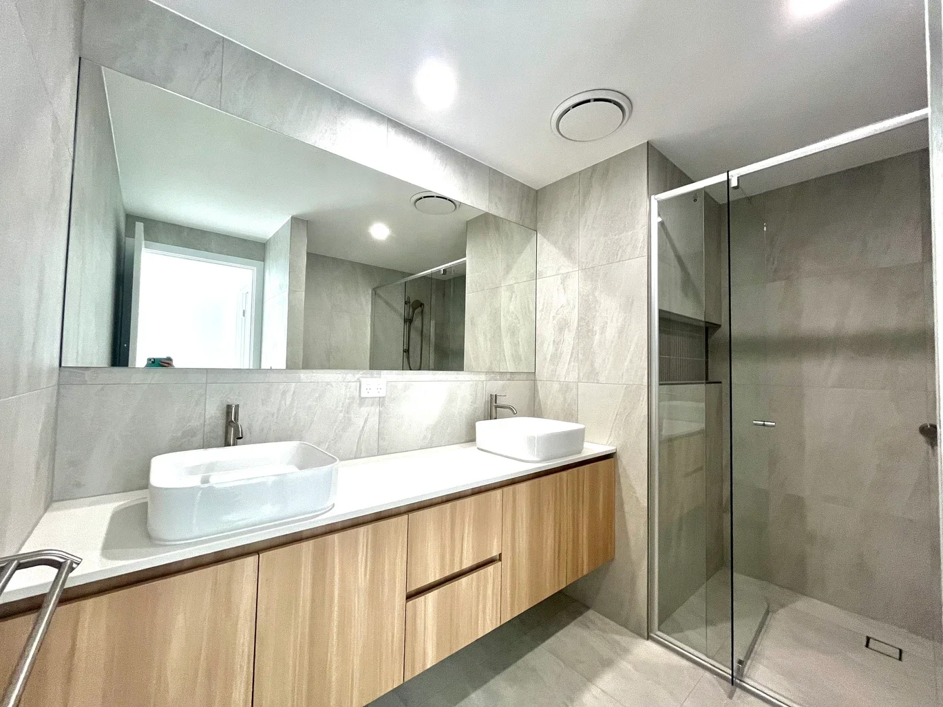Modern bathroom with double vanity sinks, large mirror, and walk-in shower with glass door.