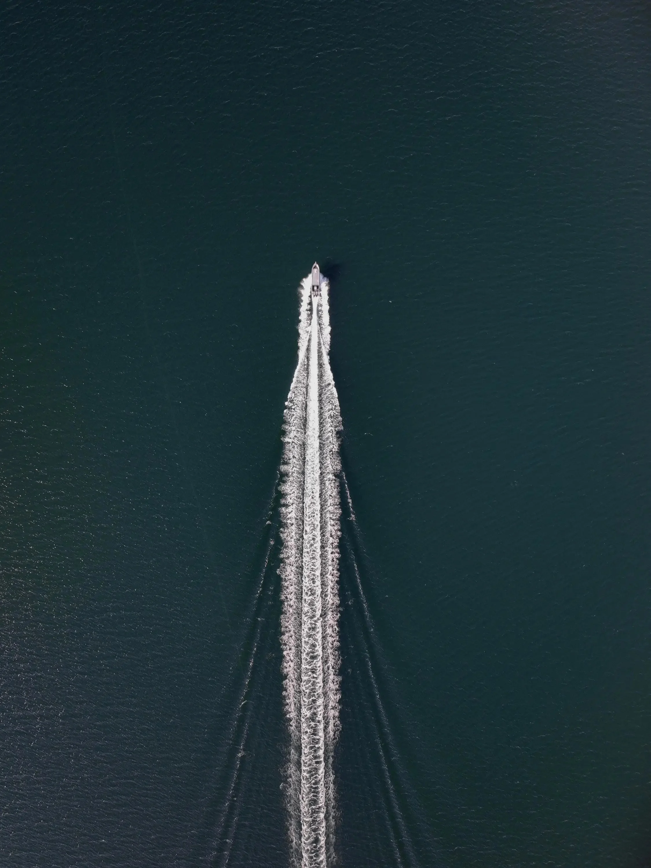 Aerial view of a boat creating a wake in dark green water.