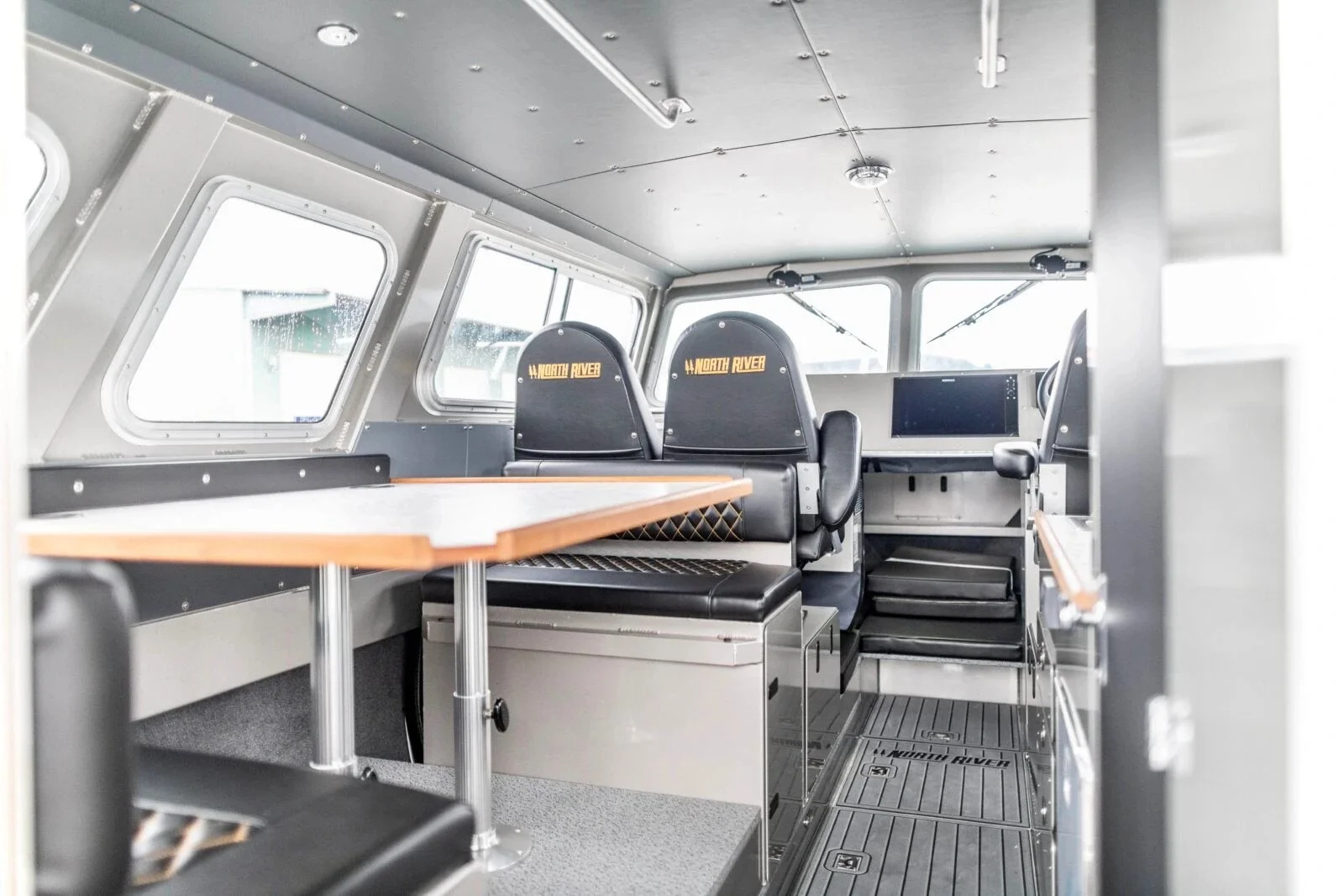 Interior of a North River boat showing seating, a table, windows, and a dashboard area.