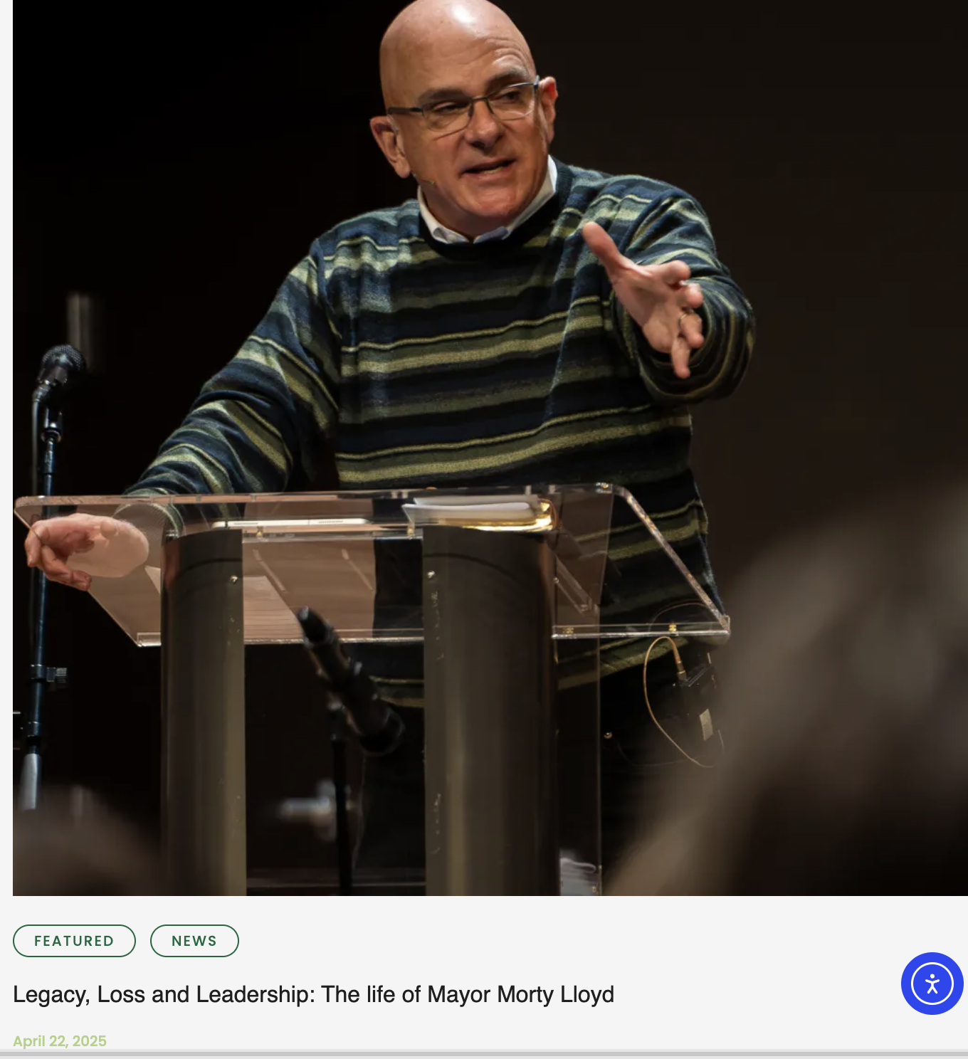 A man delivering a speech at a podium with a microphone, gesturing with his right hand, during an event titled "Legacy, Loss and Leadership: The life of Mayor Morty Lloyd" on April 22, 2025.