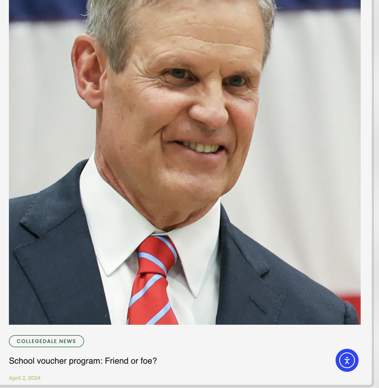 A smiling middle-aged man with gray hair, wearing a dark suit, white shirt, and red striped tie, posing for a photo.