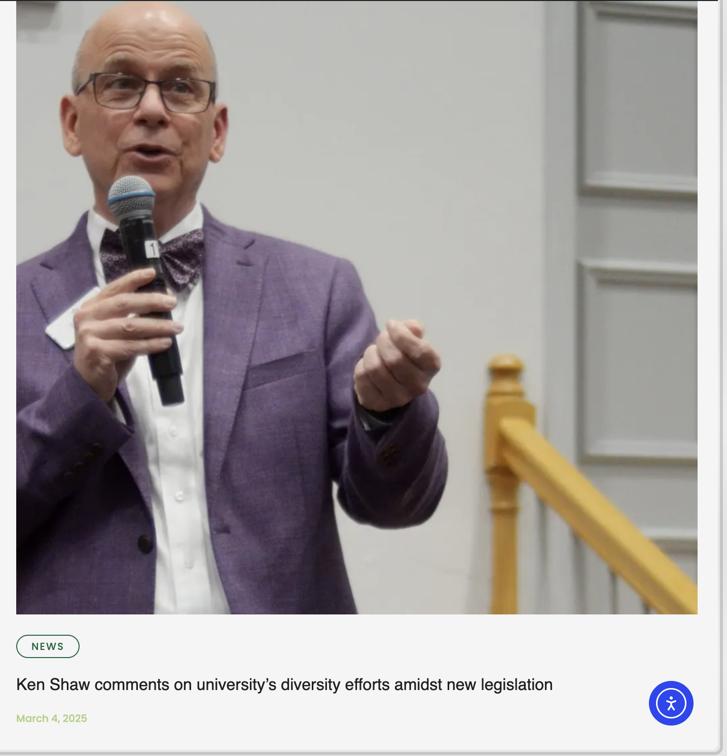 A man in a purple suit, white shirt, and bow tie is speaking into a microphone.