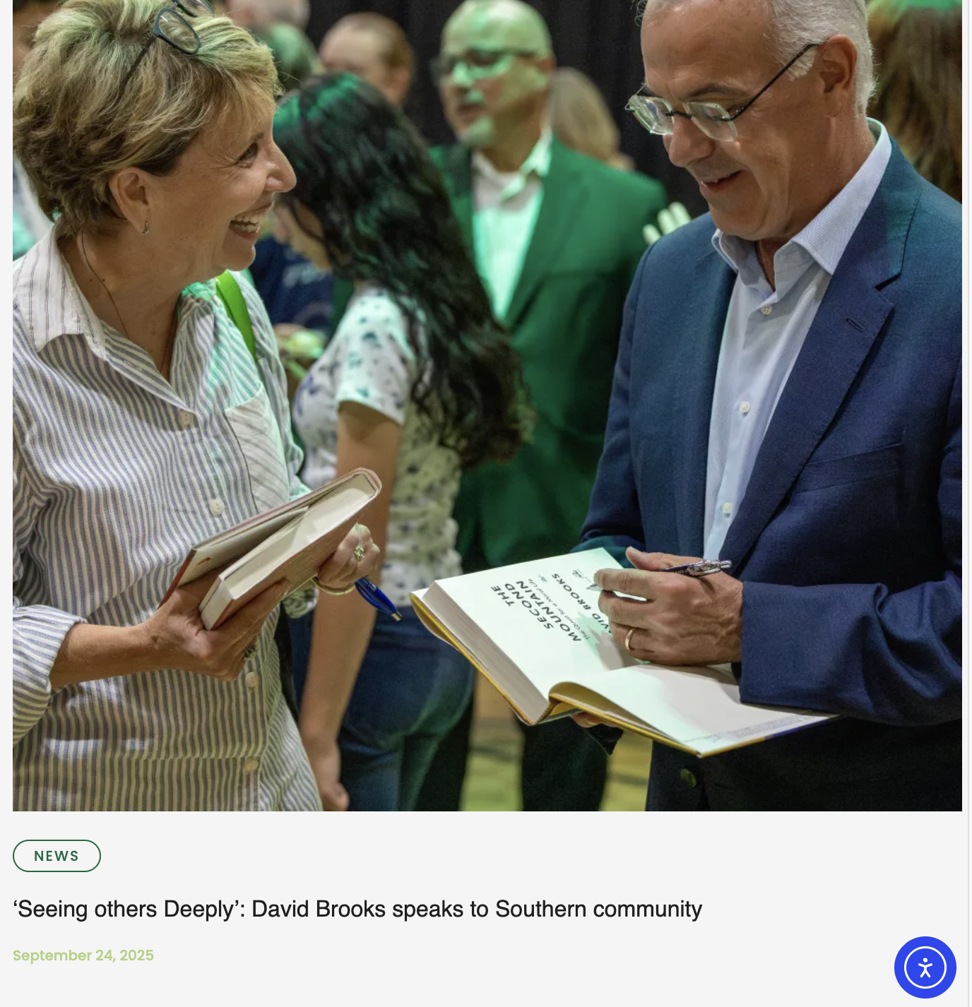 David Brooks, a man in a blue blazer with glasses, is speaking to a woman with short blonde hair in a striped shirt, while holding a book. They are engaged in conversation at a gathering or event, with multiple people in the background.