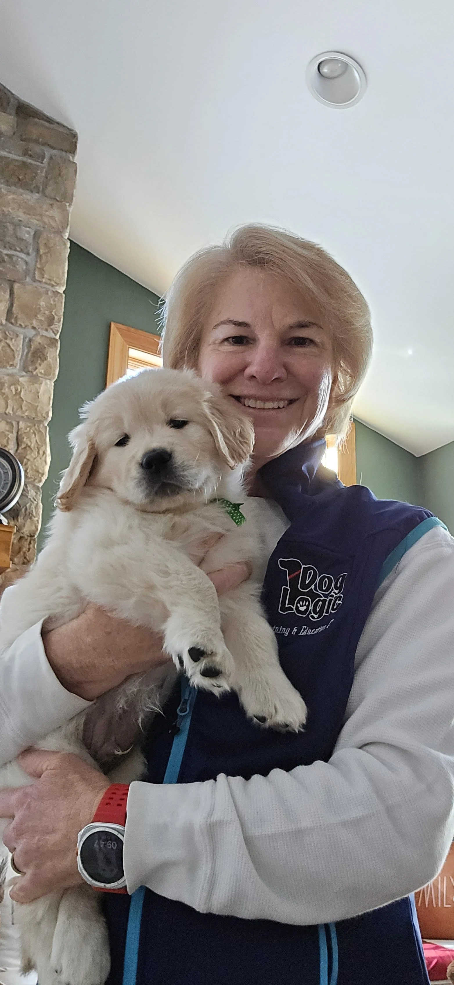 A woman with short blonde hair smiling while holding a fluffy golden retriever puppy indoors.