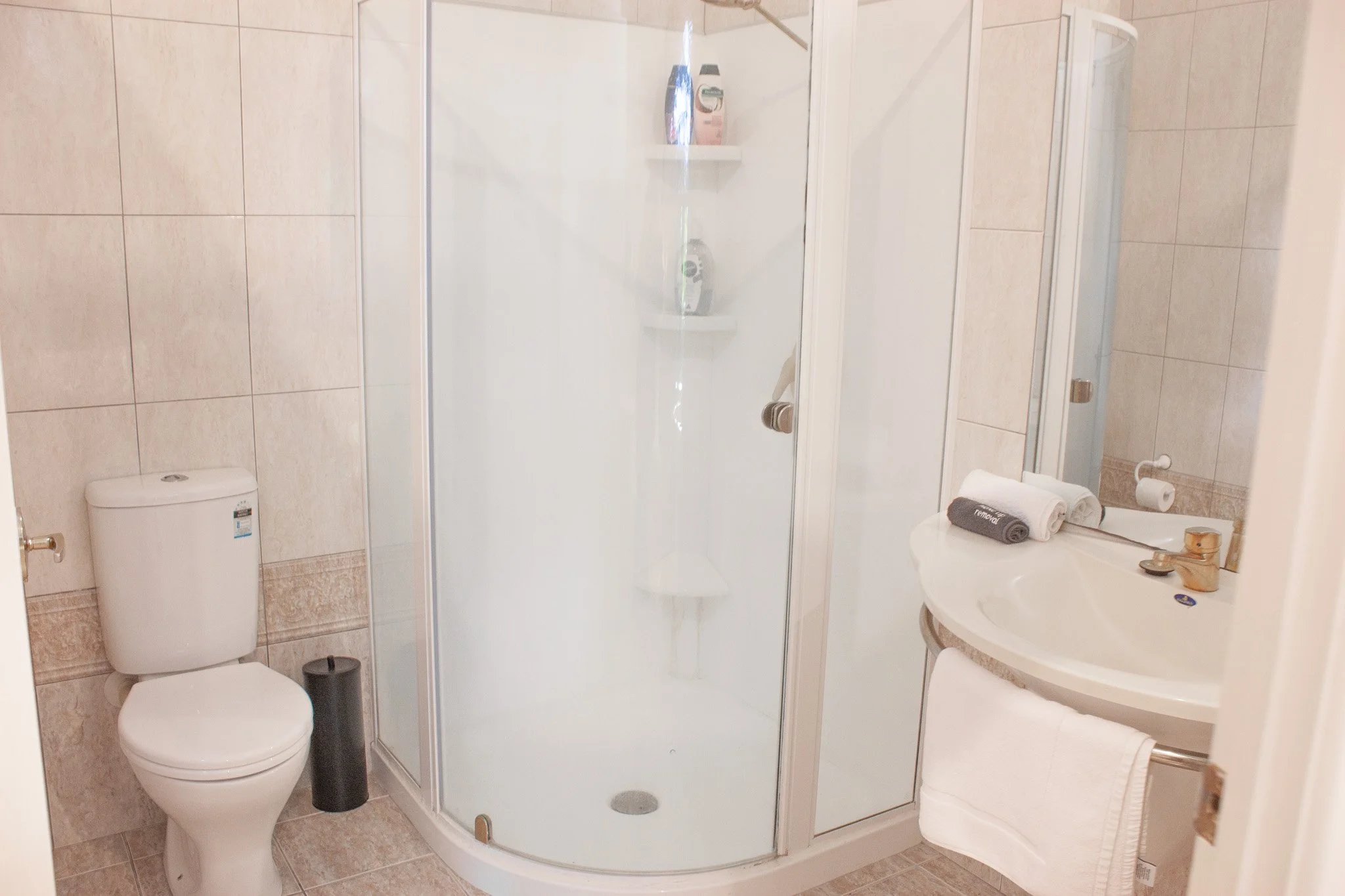 Bathroom with a toilet, a shower enclosure, and a sink with rolled towels and a mirror.