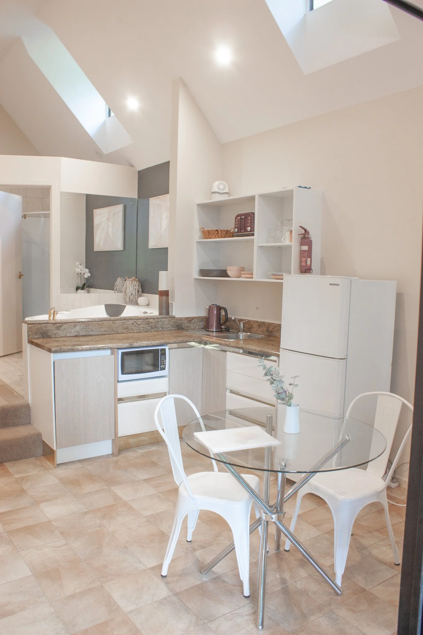 Kitchen with glass dining table, white chairs, microwave, refrigerator, open shelving, and kitchen appliances.