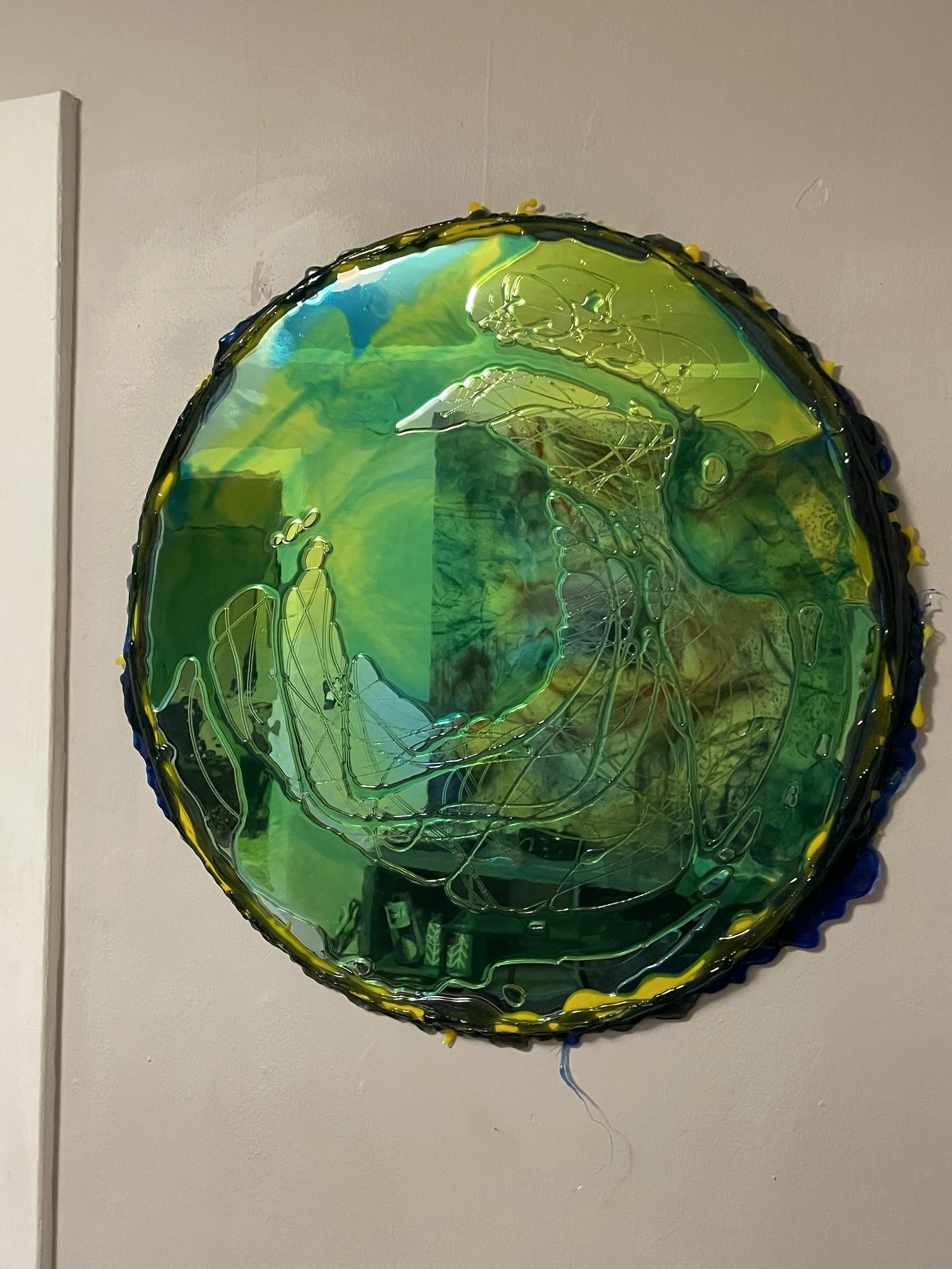 Colorful resin mirror artwork resembling a circular abstract with green, yellow, and blue hues, featuring dynamic lines and textures on a wall.