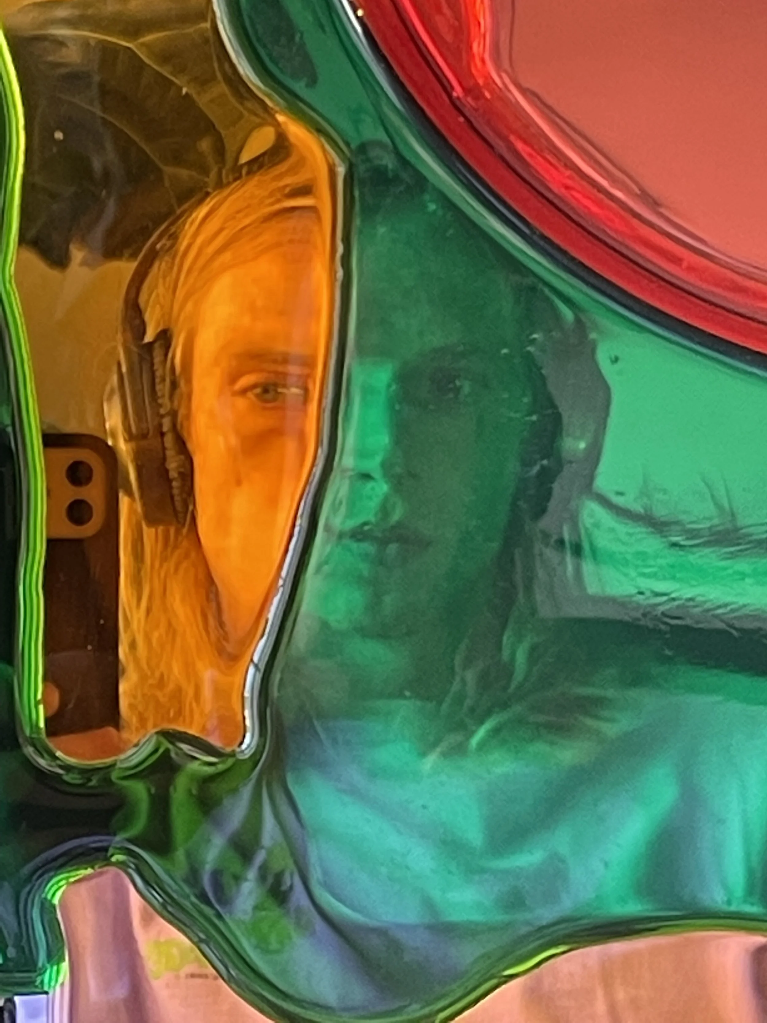 Close-up of colorful resin mirror art with a reflection of a person holding a camera, partially visible through the green and orange resin.