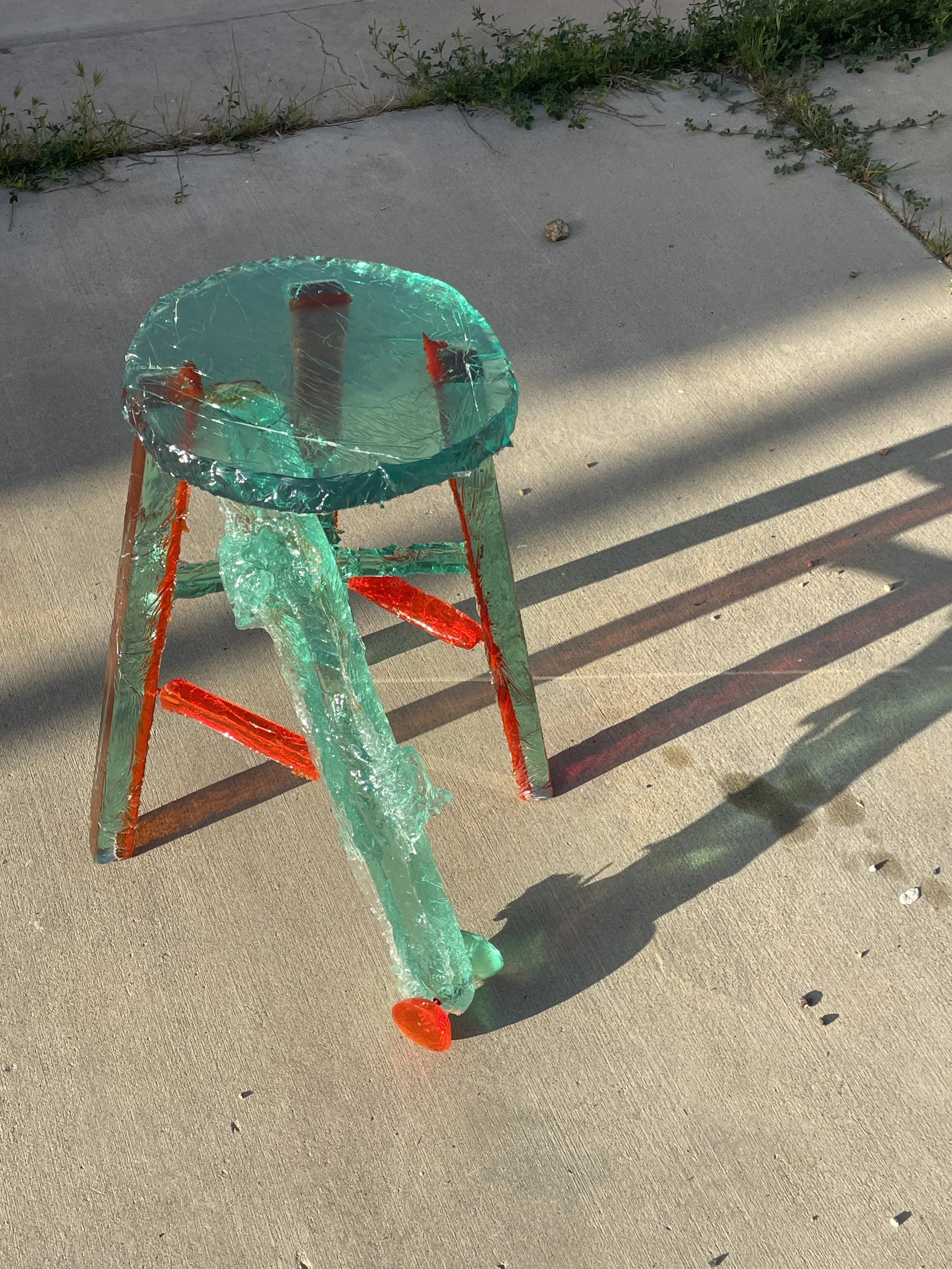 A resin chair with a glass-like top casting a shadow on a concrete surface.
