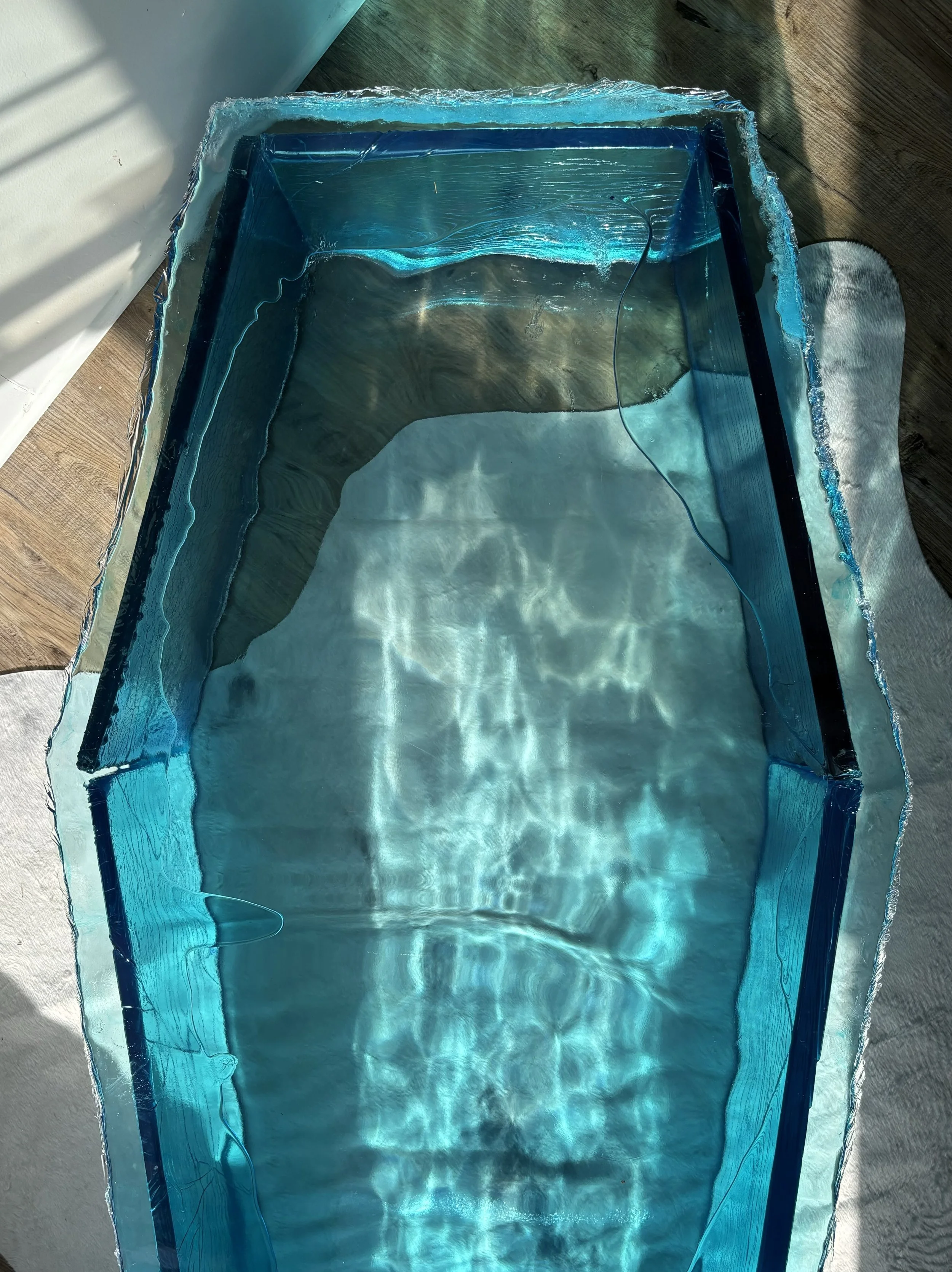 An ice like resin coffin sculpture with sunlight creating ripples and reflections on the surface.