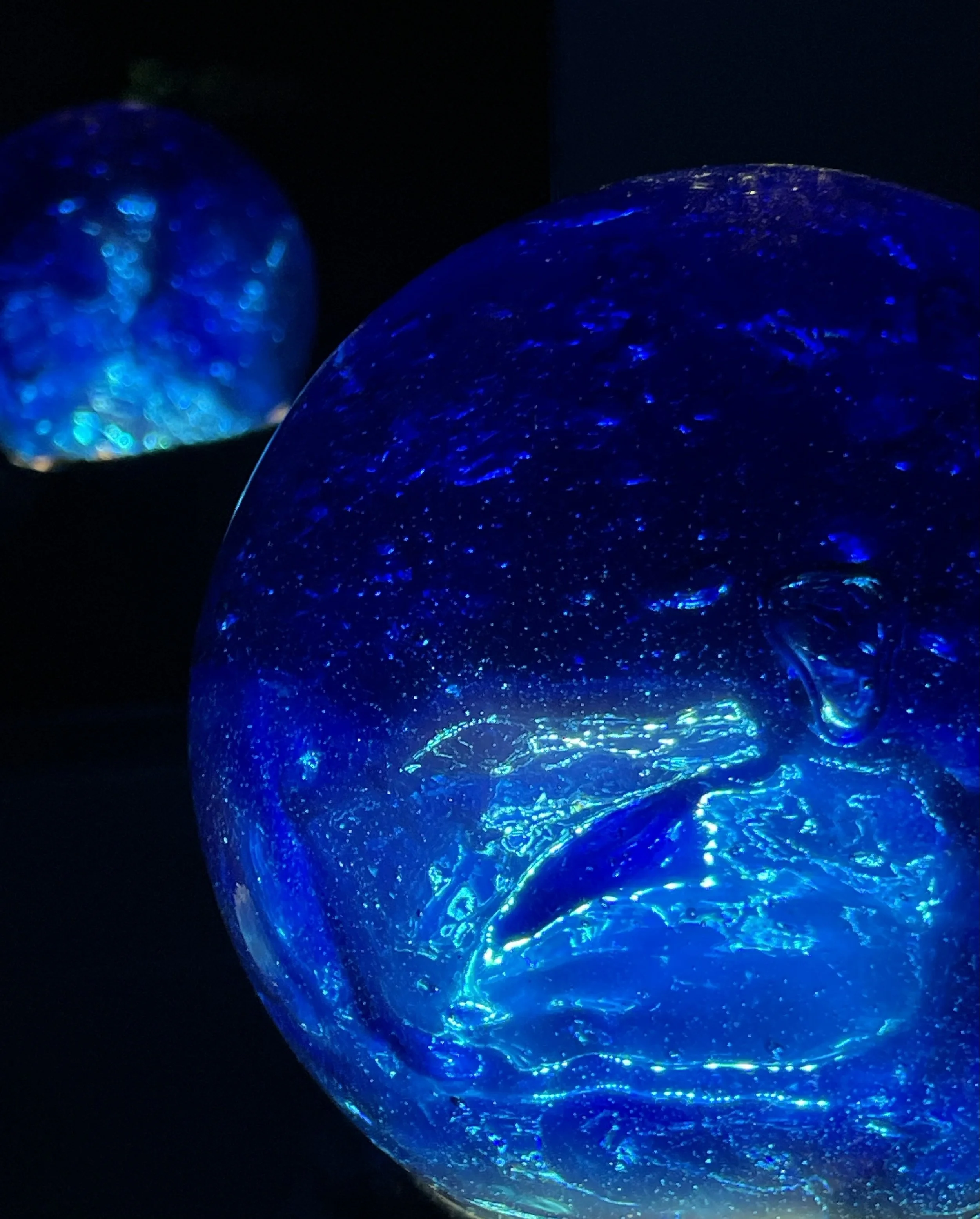 Two blue resin pondering orbs with swirling patterns inside, set against a dark background.