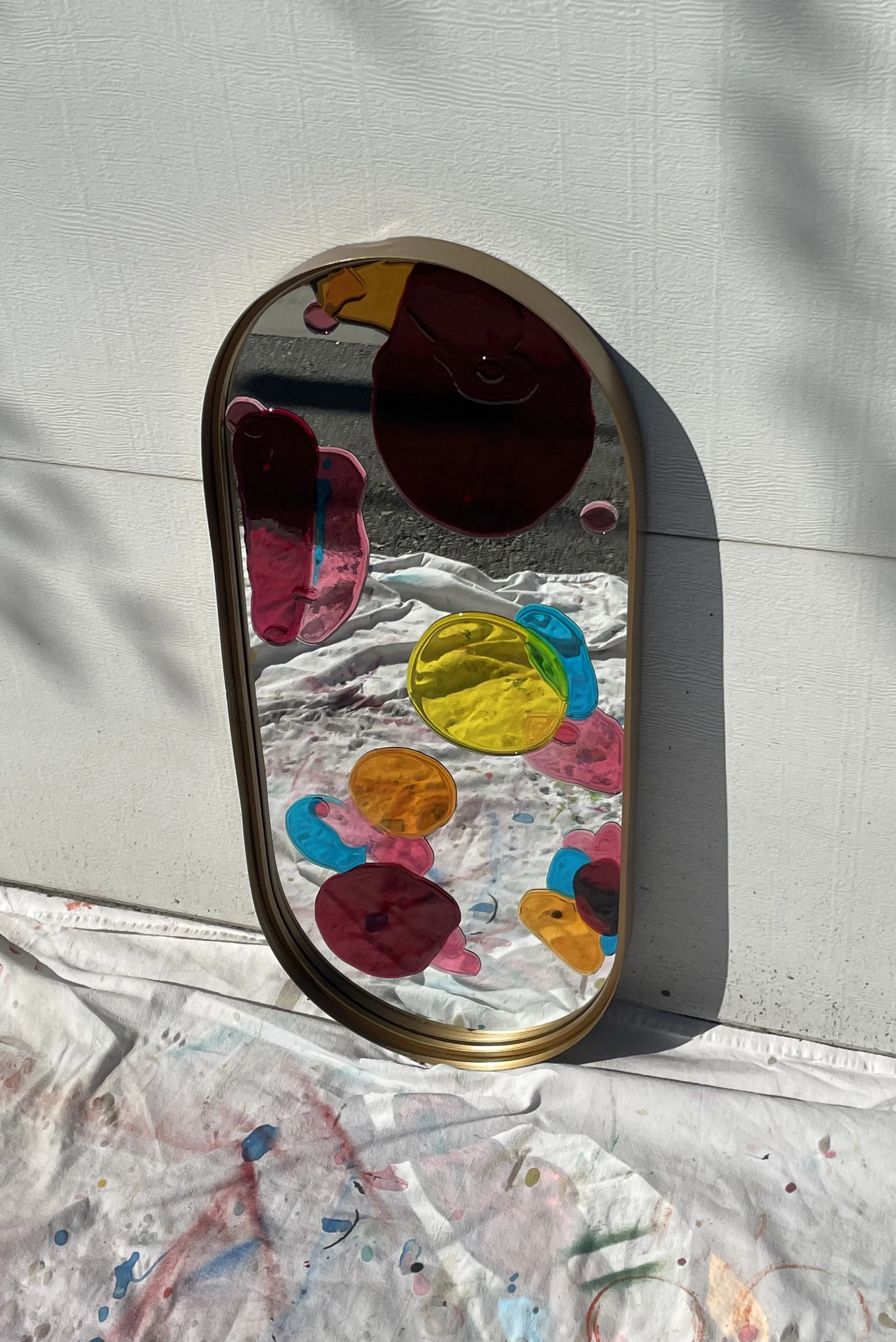 Colorful abstract resin mirror leaning against a wall outdoors on a white cloth.