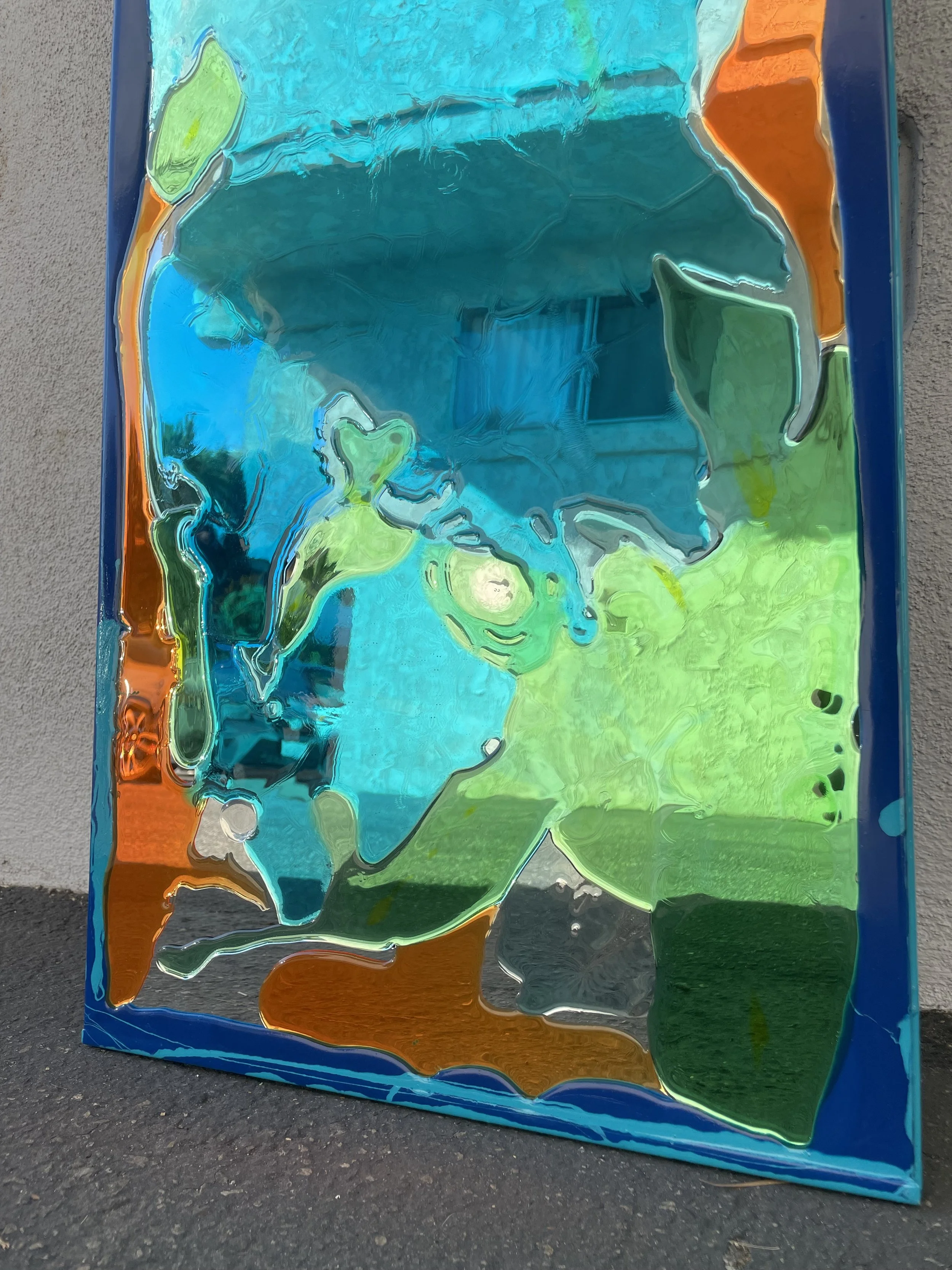 Colorful resin mirror with abstract green, blue, orange, and yellow shapes, leaning against a wall.