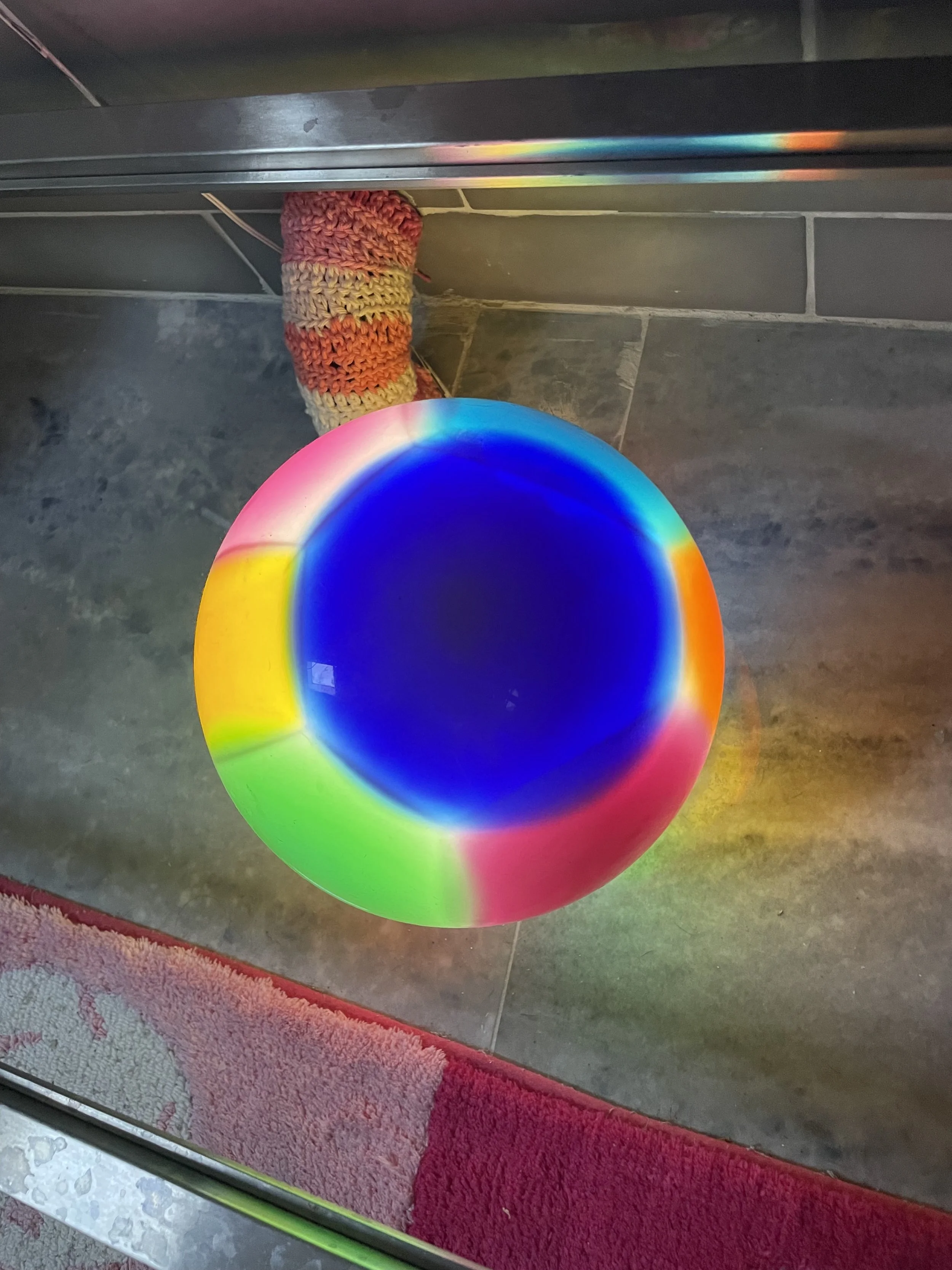 A colorful resin ball with rainbow hues, placed on a marble surface reflecting the colors.