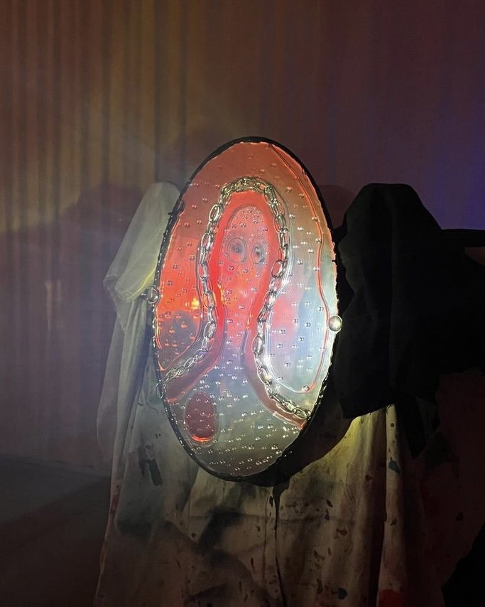 An oval shaped mirror with a chain person and resin, with light reflecting off