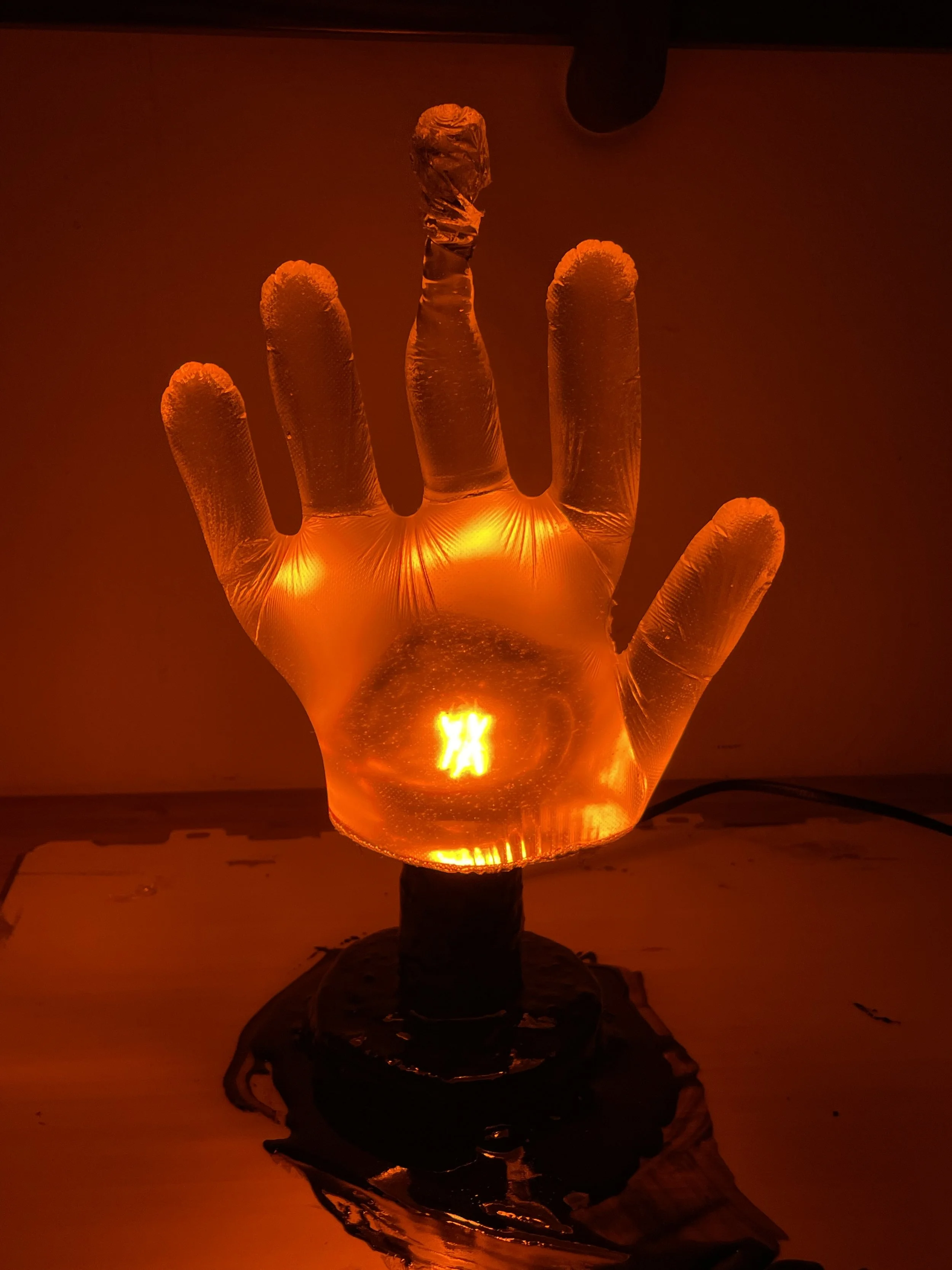 A glowing hand-shaped resin lamp with a fiery red-orange light, mounted on a dark base, illuminating a dim room.