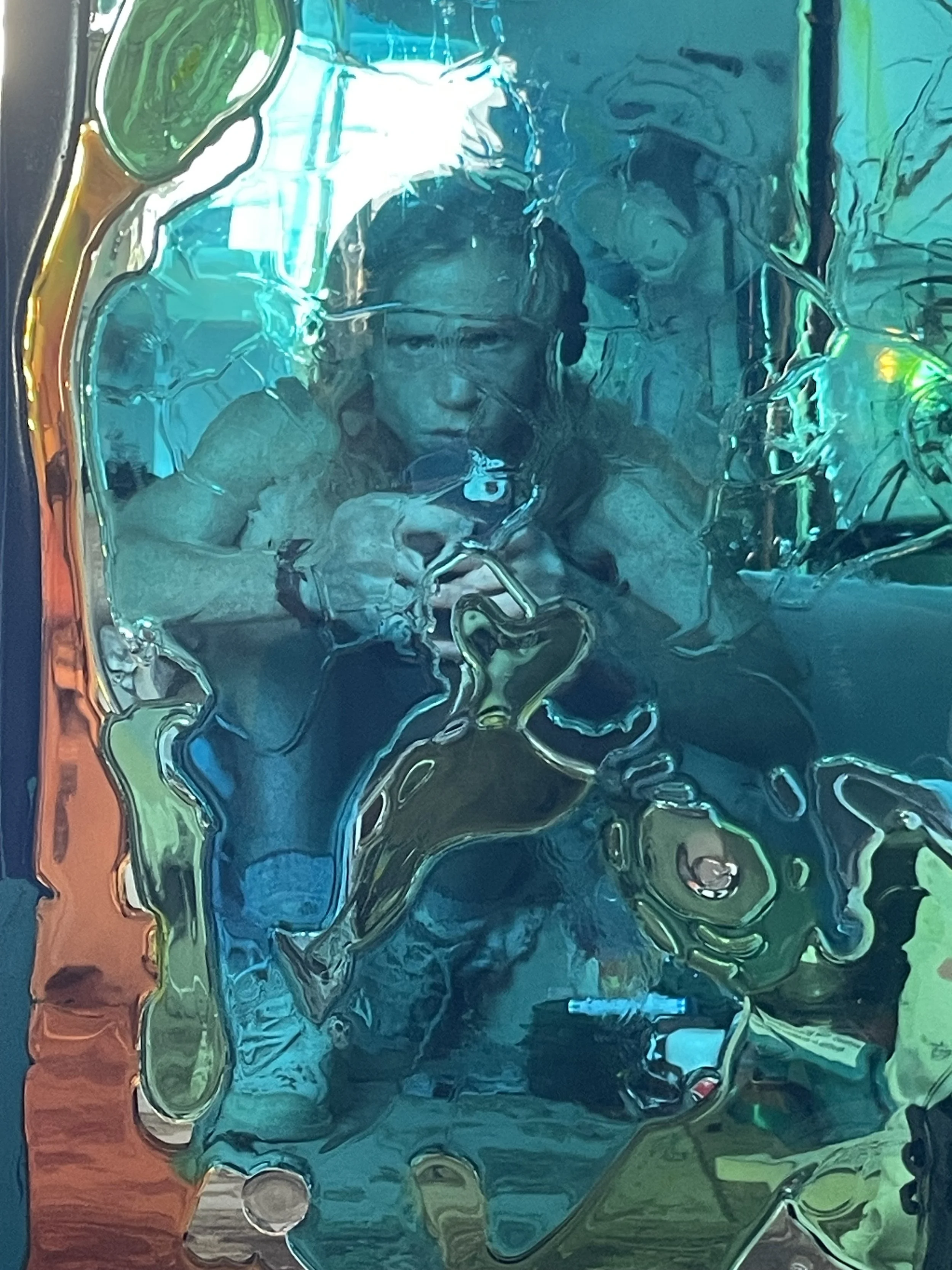 A person taking a photo through a distorted resin mirror, causing the image to appear wavy and abstract with hues of blue, green, and orange.