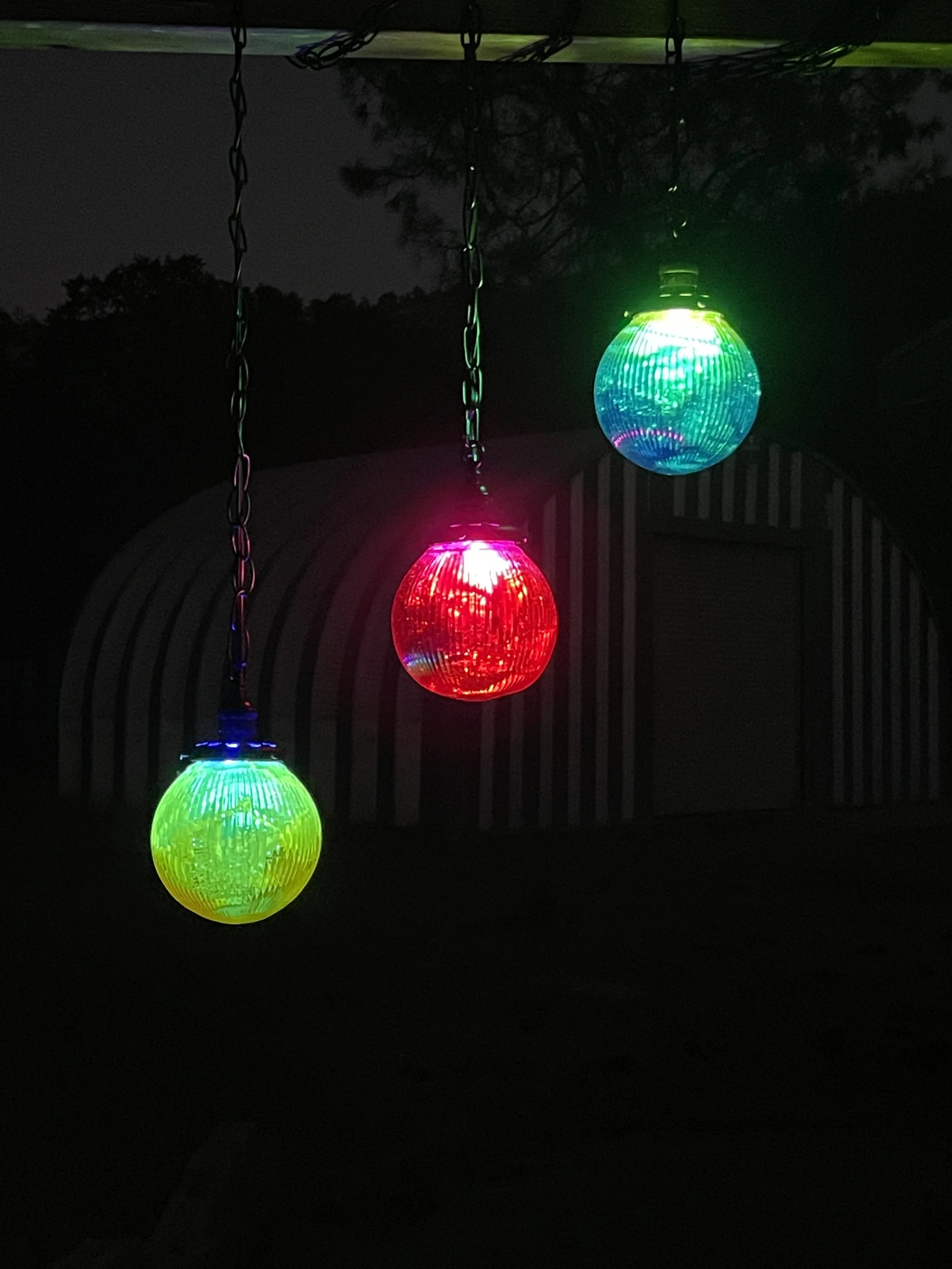 Three colorful hanging resin lights in green, red, and blue illuminate the dark outdoor area at night.