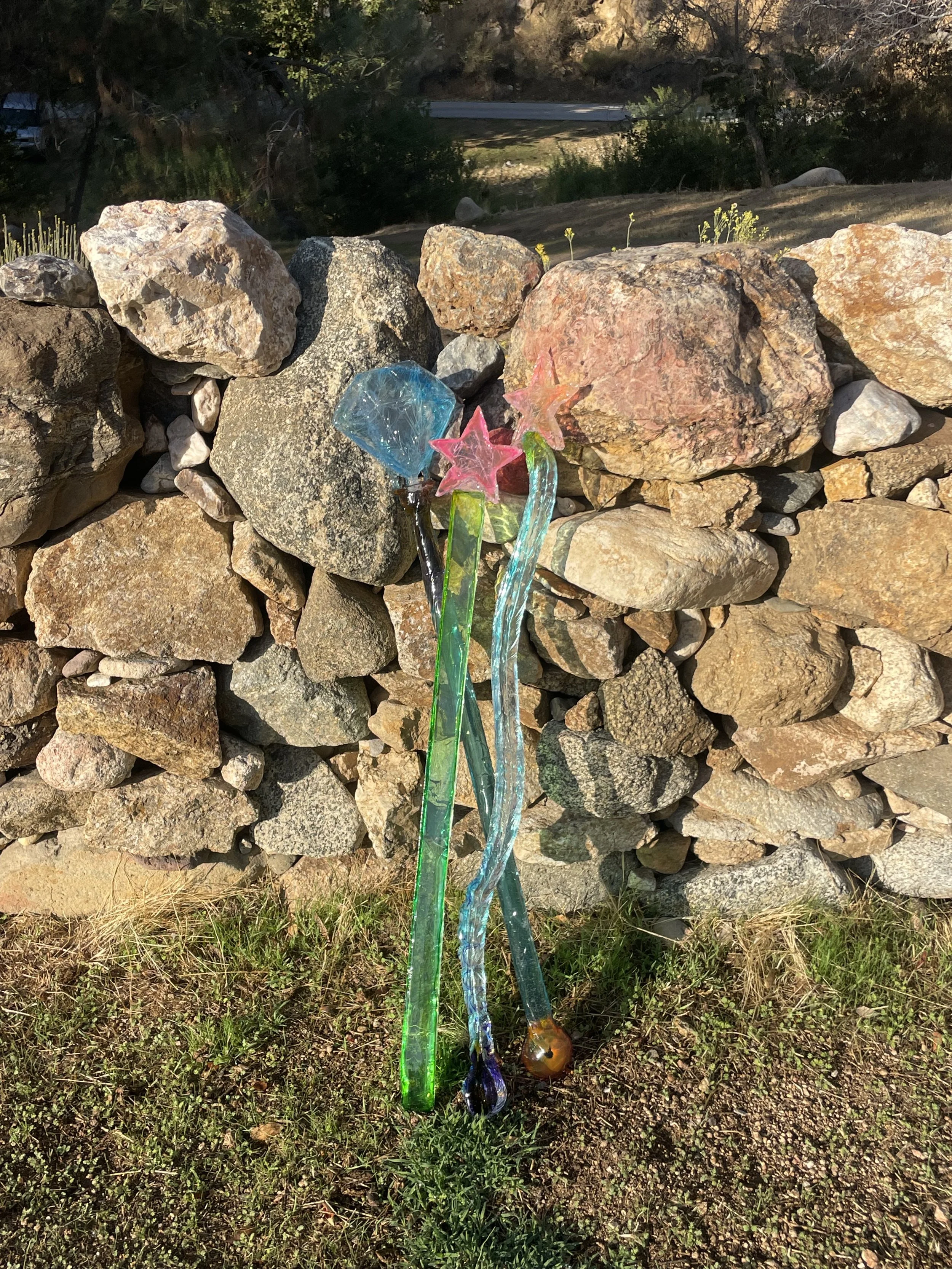 Colorful resin magic wands with stars and a diamond shape on top leaning against a stone wall.