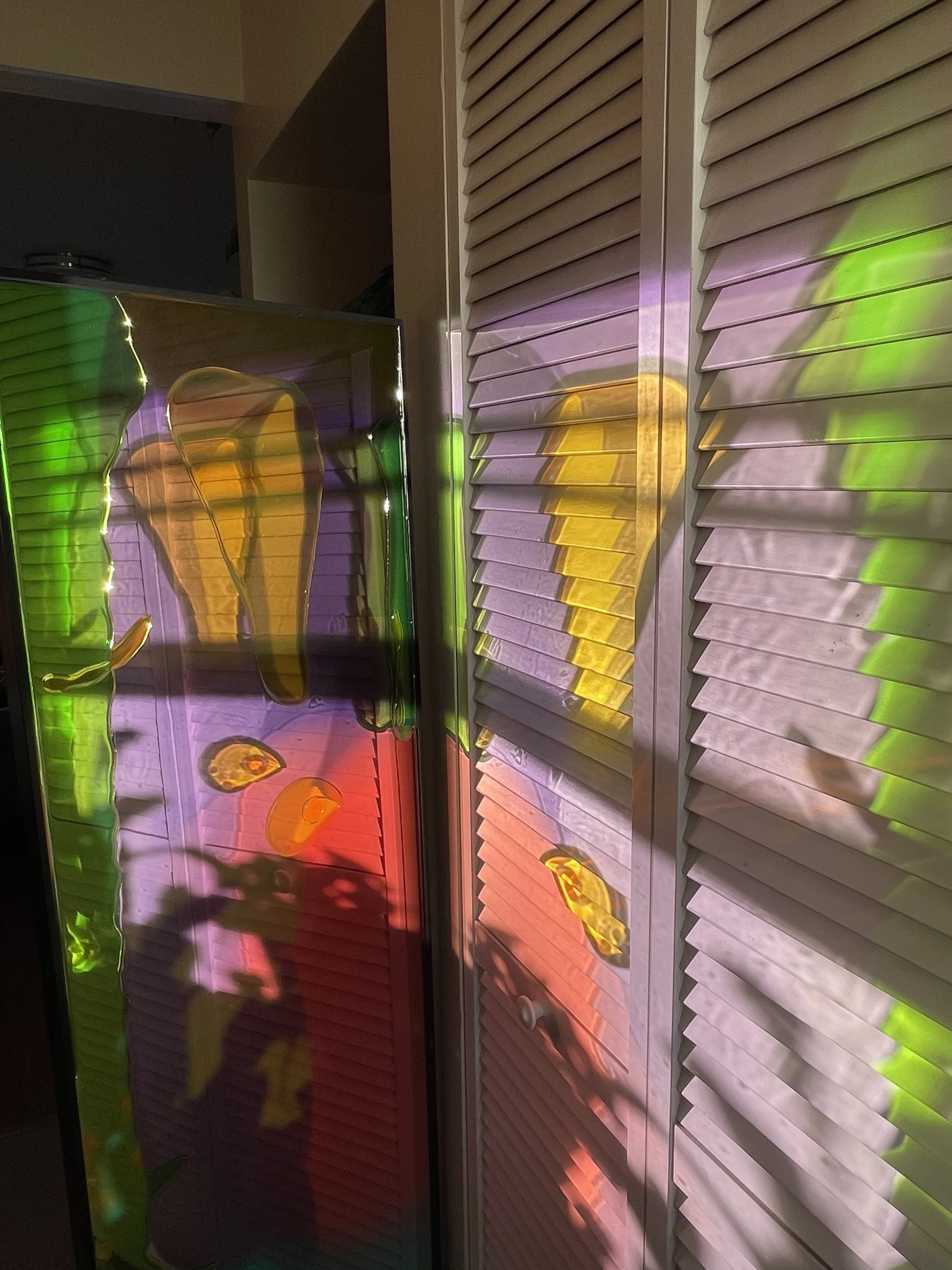 Colorful reflections of resin mirror on white closet louvered doors with shadows.
