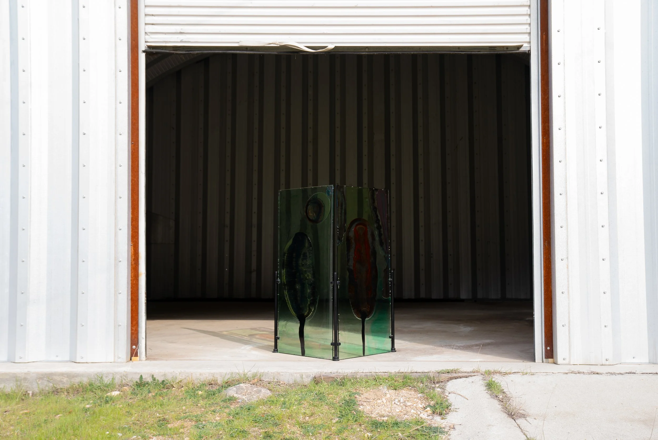 A metal storage shed with its door open. Inside, a resin art piece with abstract shapes and dark colors stands on the concrete floor.