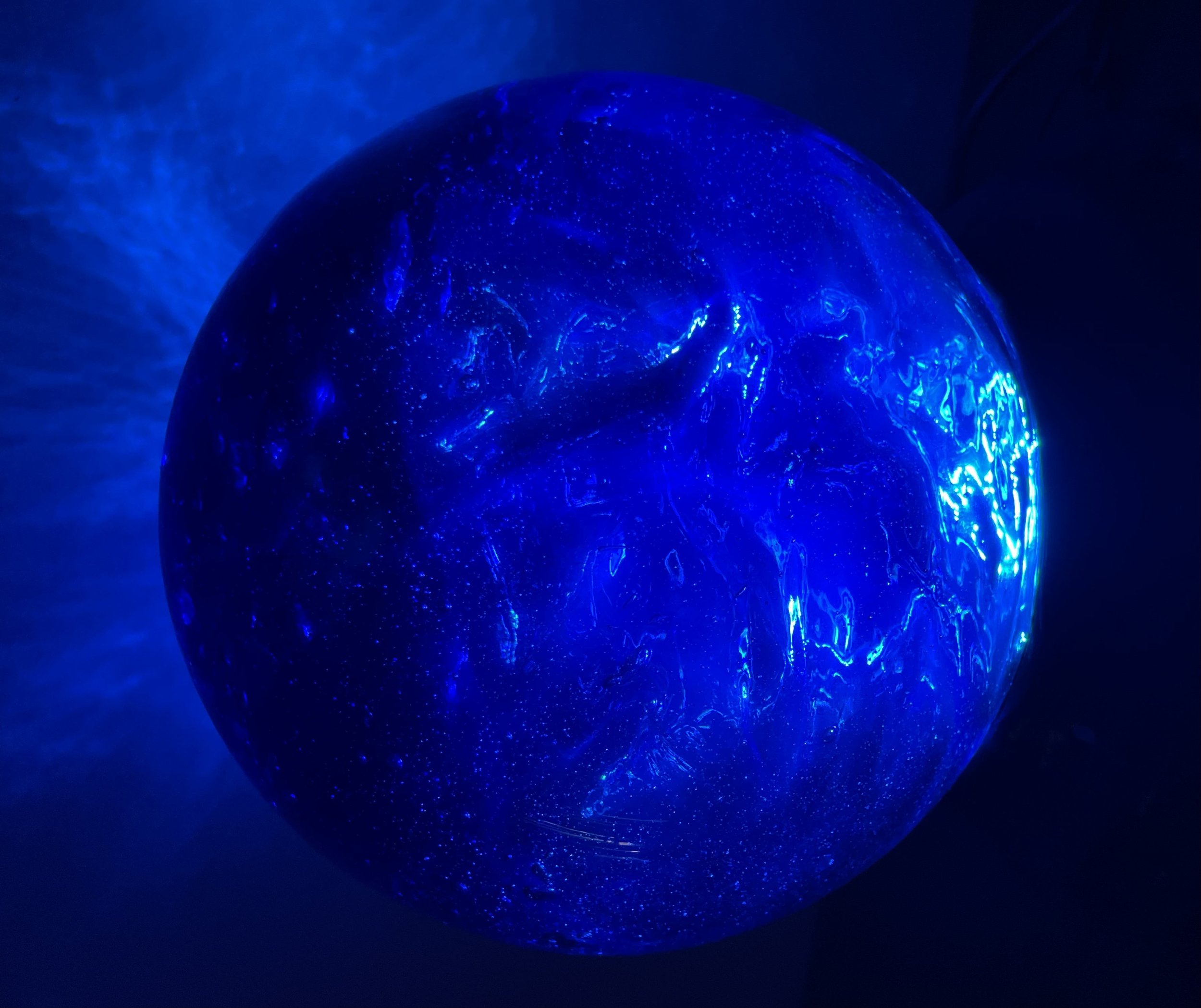 A glowing blue resin pondering orb with swirling patterns and tiny white specks resembling stars, casting a blue light and shadows.