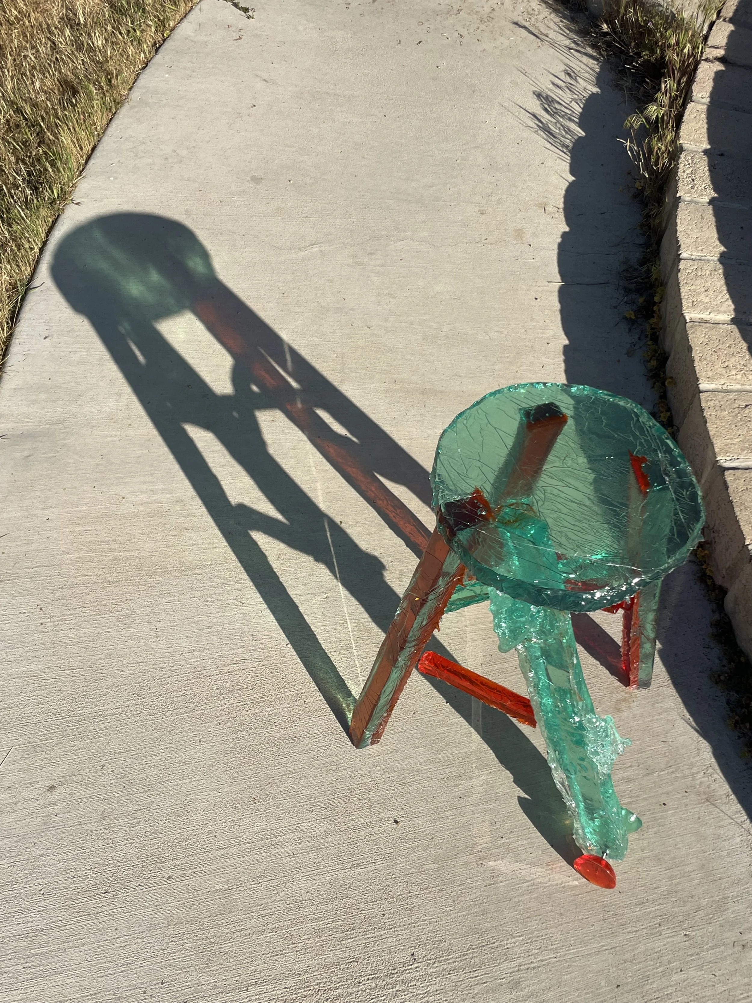 A glass sculpture of a bicycle casting a shadow on a concrete sidewalk next to a grassy area and a brick border.
