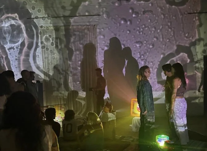Group of people in an art installation with colorful projections and shadows on the walls.