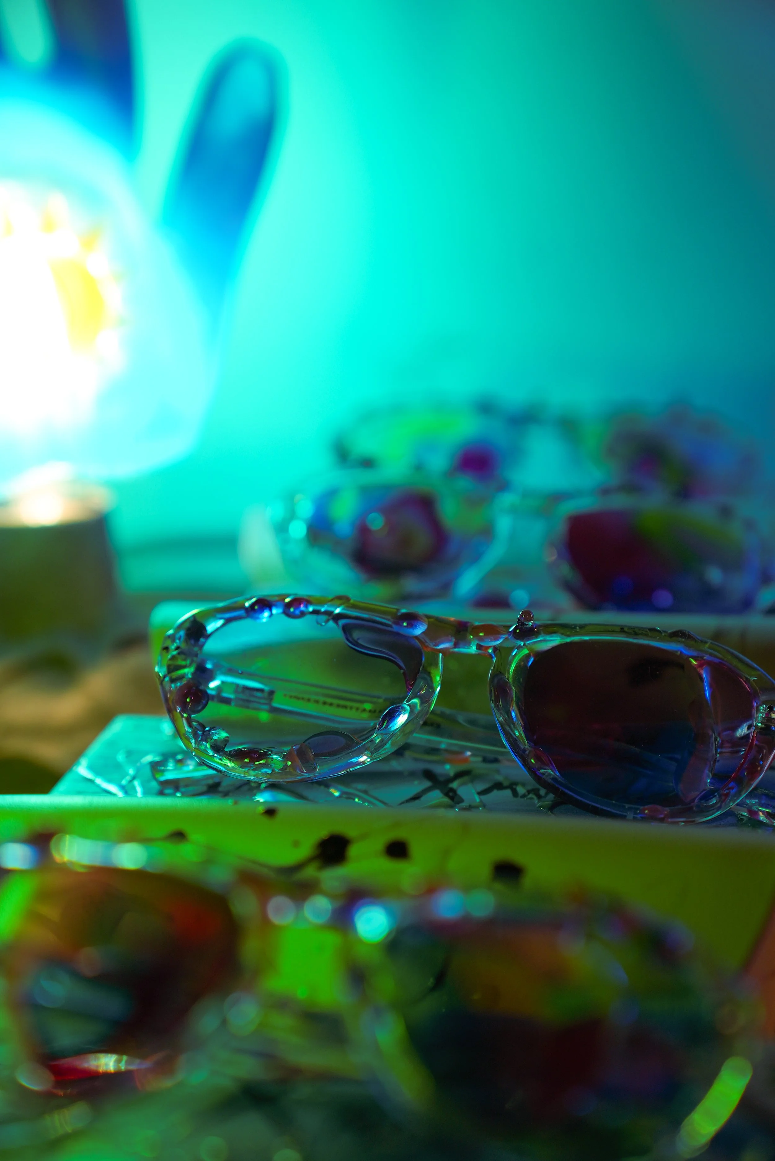 Close-up of colorful sunglasses with vibrant neon lighting, showcasing reflections on the lenses with a blurred background.