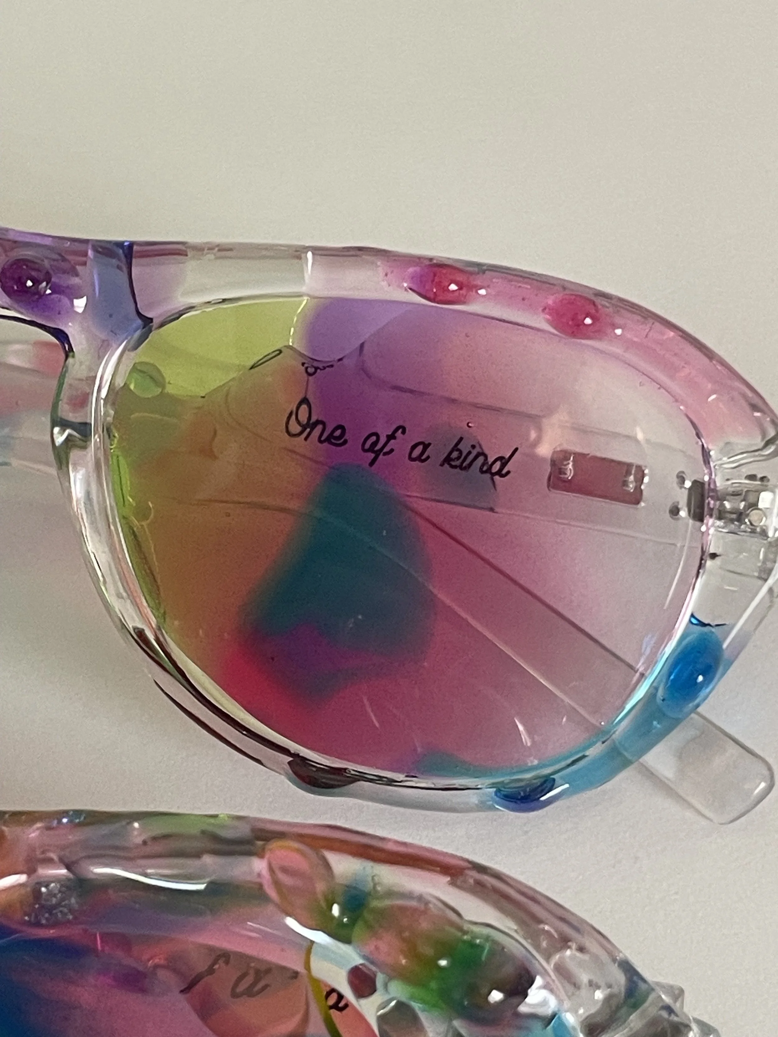 Colorful sunglasses with the phrase 'One of a kind' written on the lens.