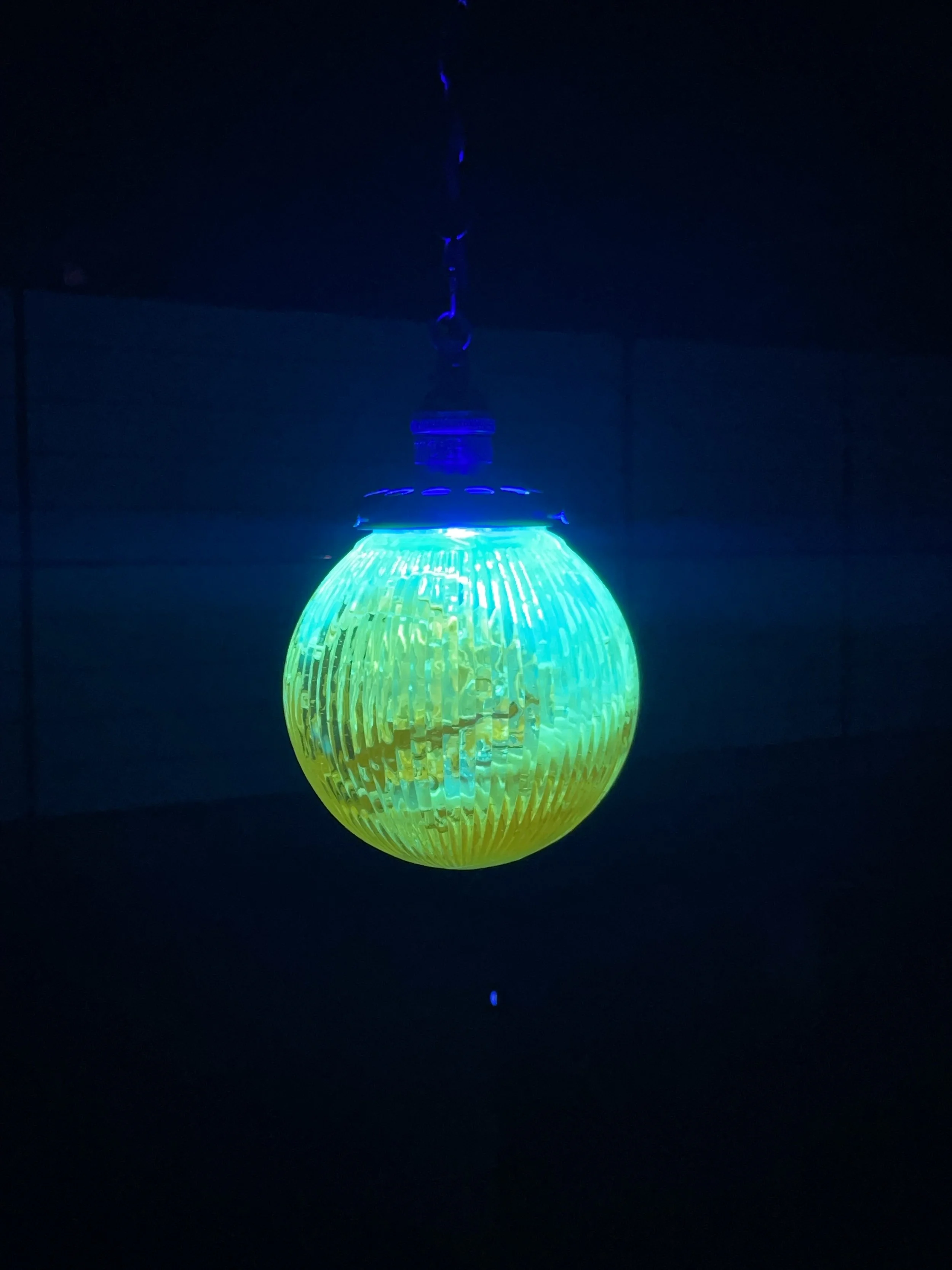 A glowing, blue and yellow resin light hanging from a chain in a dark room.