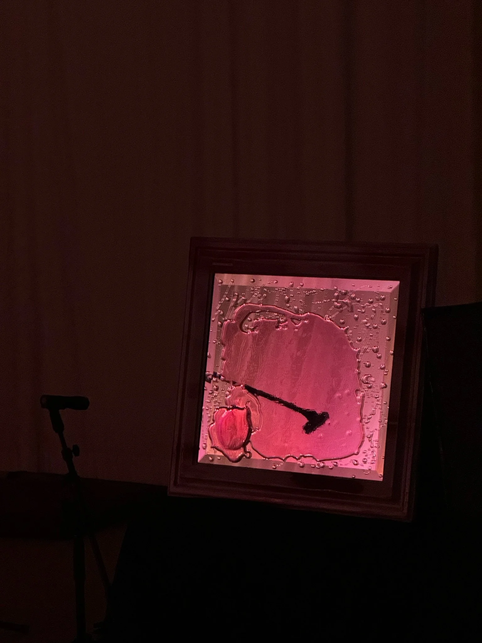 A pink resin mirror set against a dark background with a microphone stand nearby.