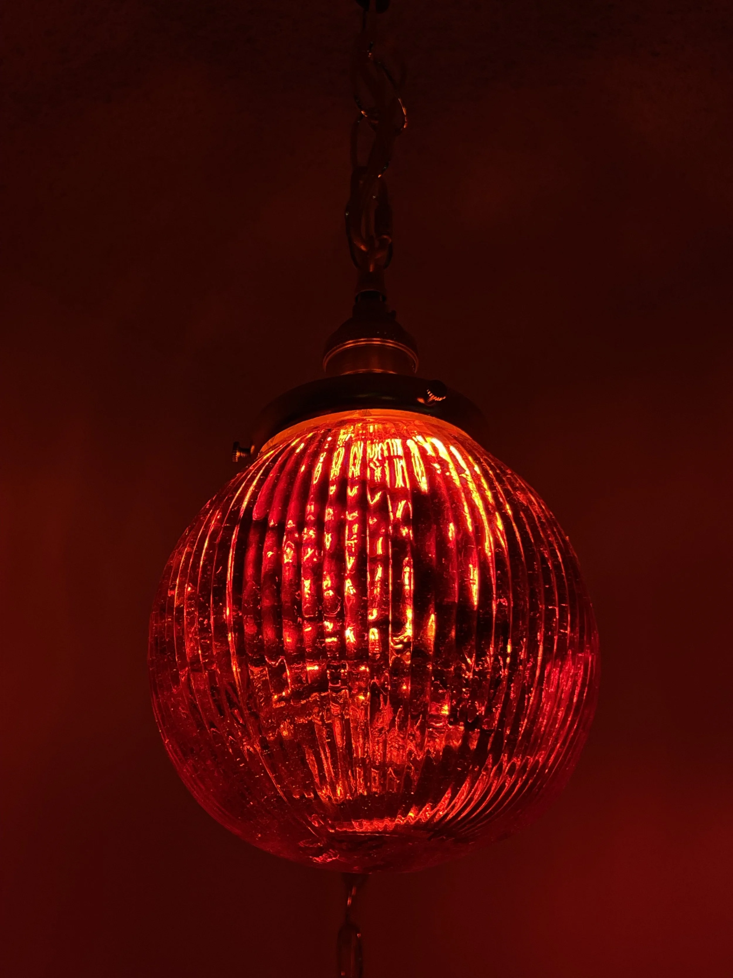 Red spherical pendant resin light fixture with vertical ridges, hanging from a chain.