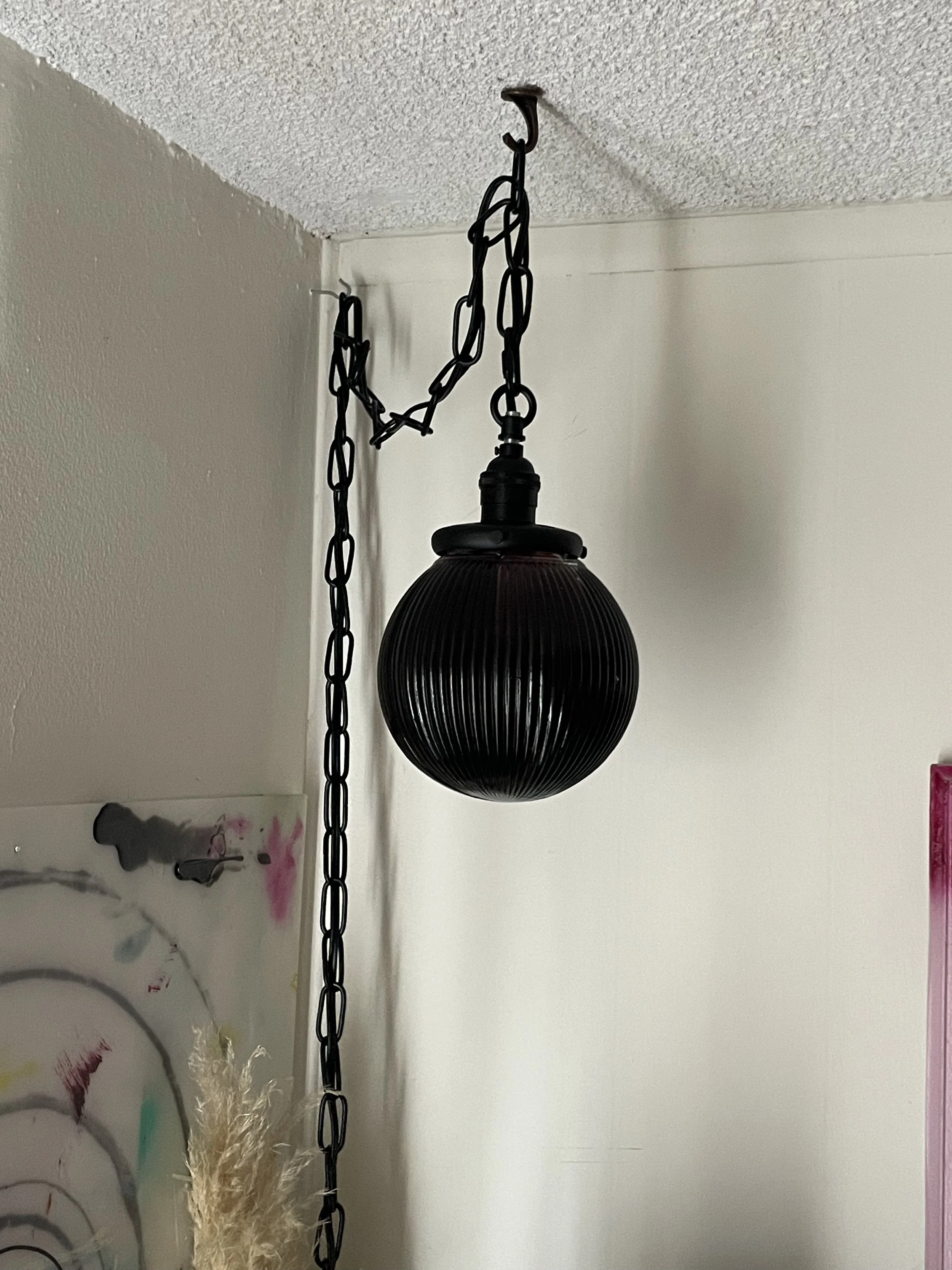 A black spherical pendant resin light hanging from a chain attached to the ceiling in a room with a textured ceiling and plain wall.