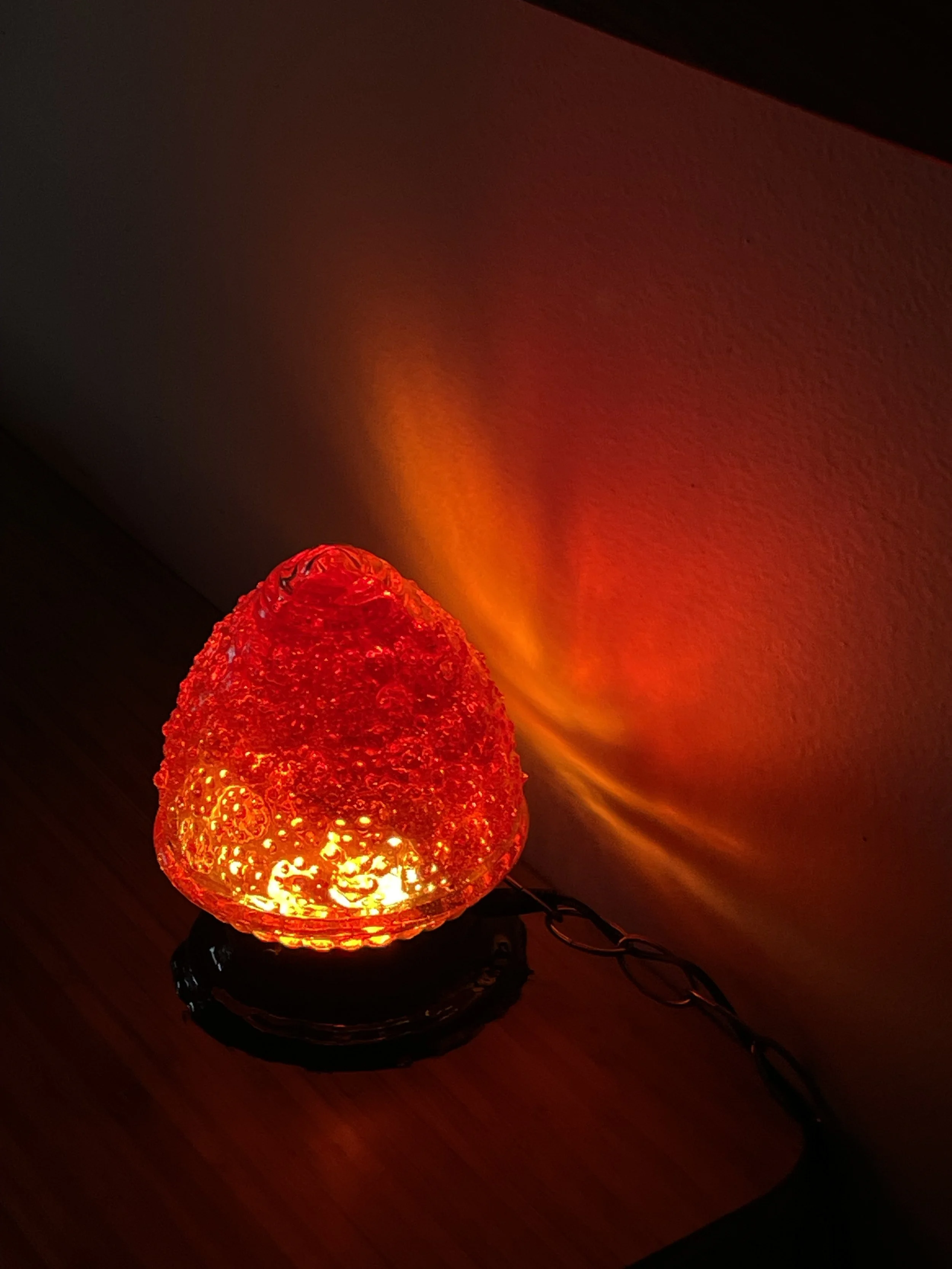 A lit red decorative resin lamp with a textured glass surface, casting a warm red glow on the wall behind it.