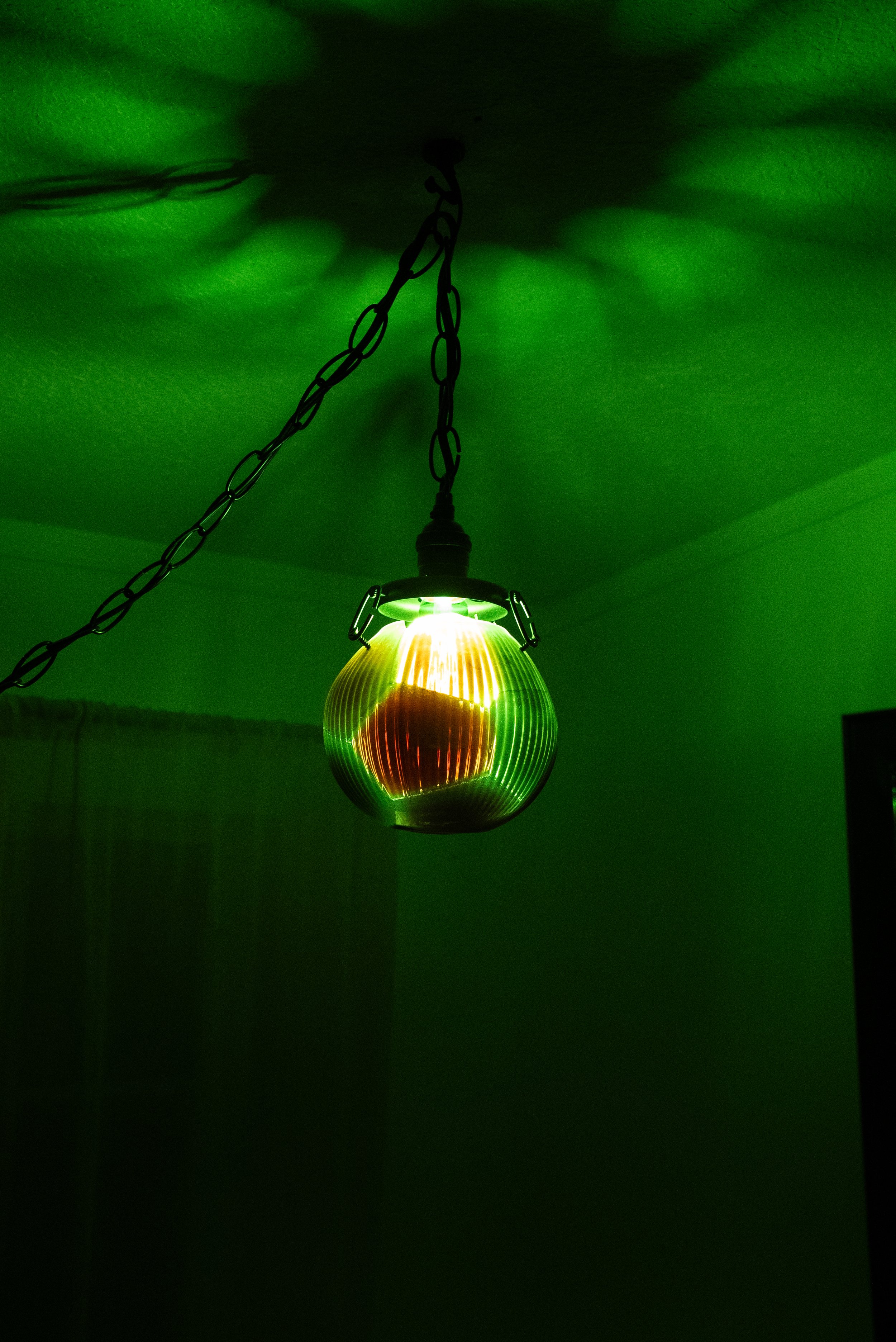 A hanging resin light fixture with a green and yellow glass shade, casting green light onto the ceiling and walls.