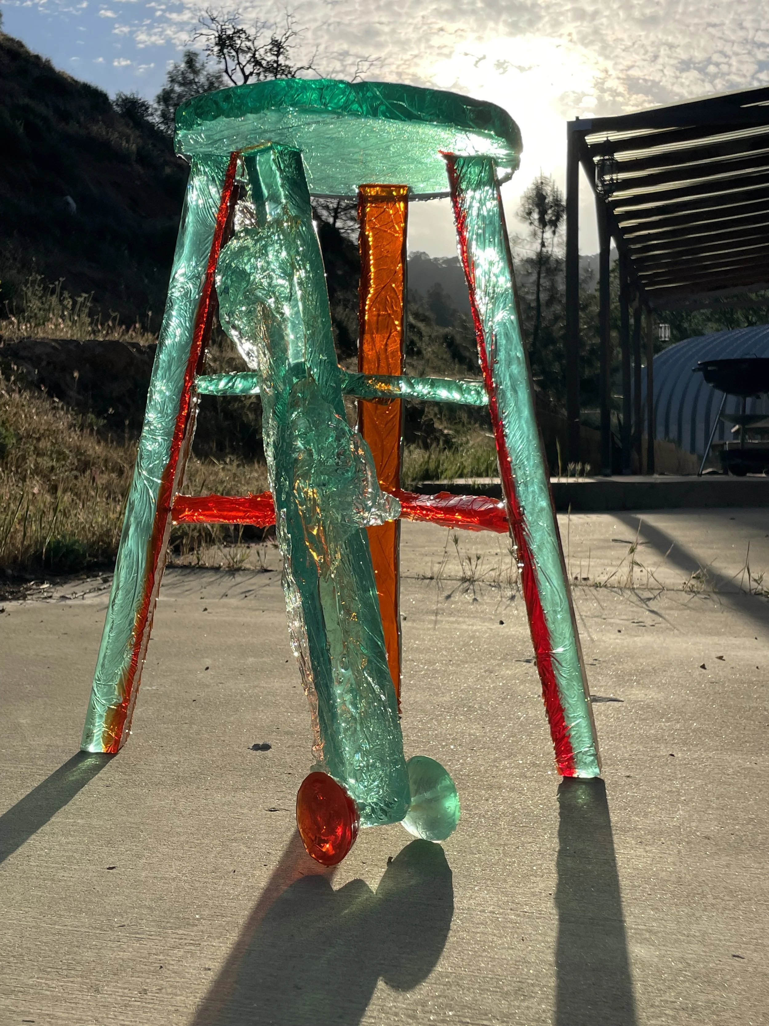 Colorful glass sculpture shaped like a small airplane, placed on a concrete surface outdoors during sunset.