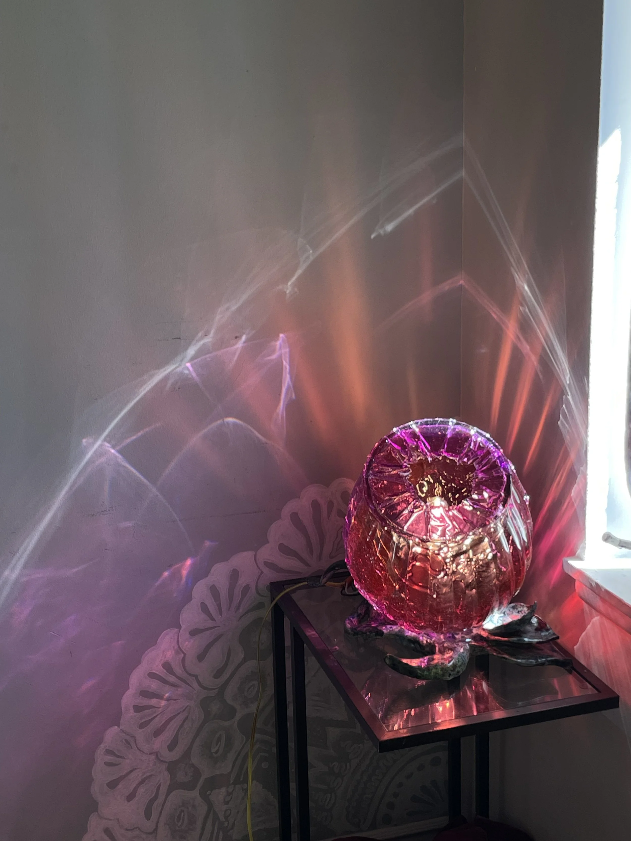 Colorful glass lamp emitting pink and purple light, casting reflections and patterns on the wall and surface nearby.