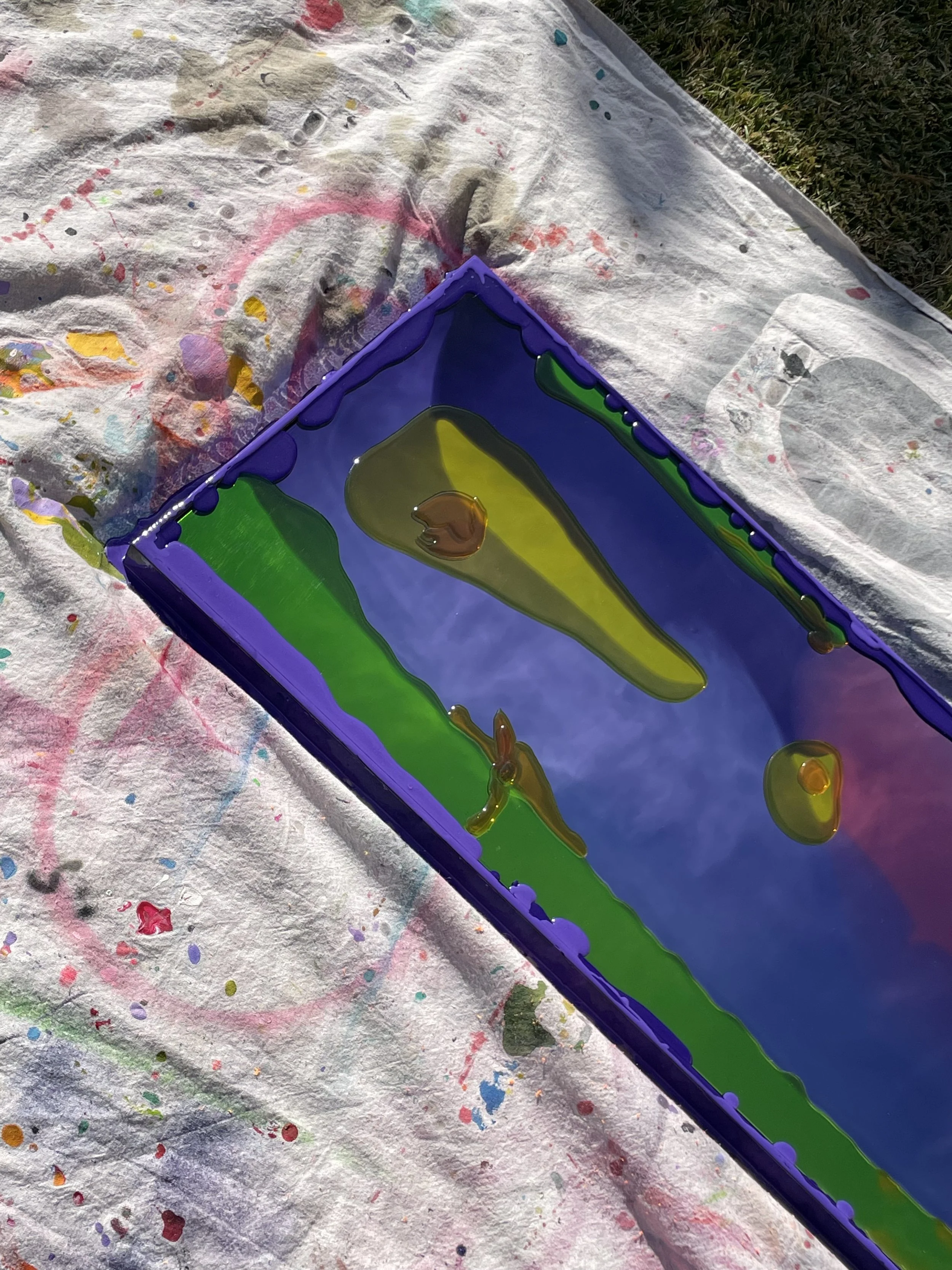 Close-up of a colorful resin mirror situated on a splattered, paint-stained drop cloth.