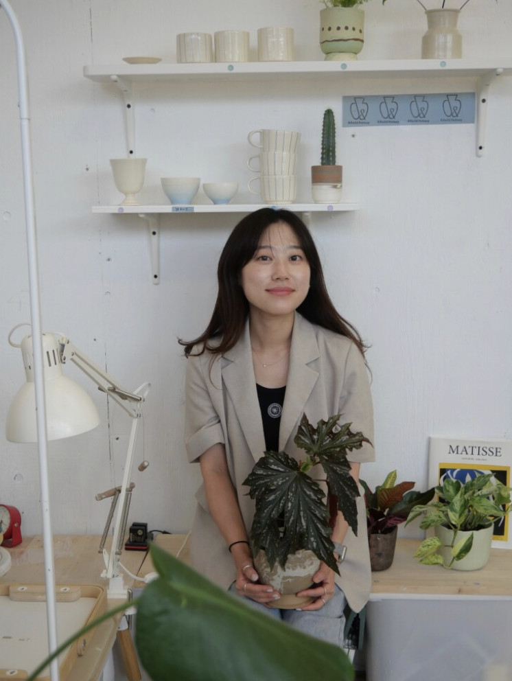 Pot Pot Studio tech Heajin posing in front of her work in the pottery studio in Toronto, ON.