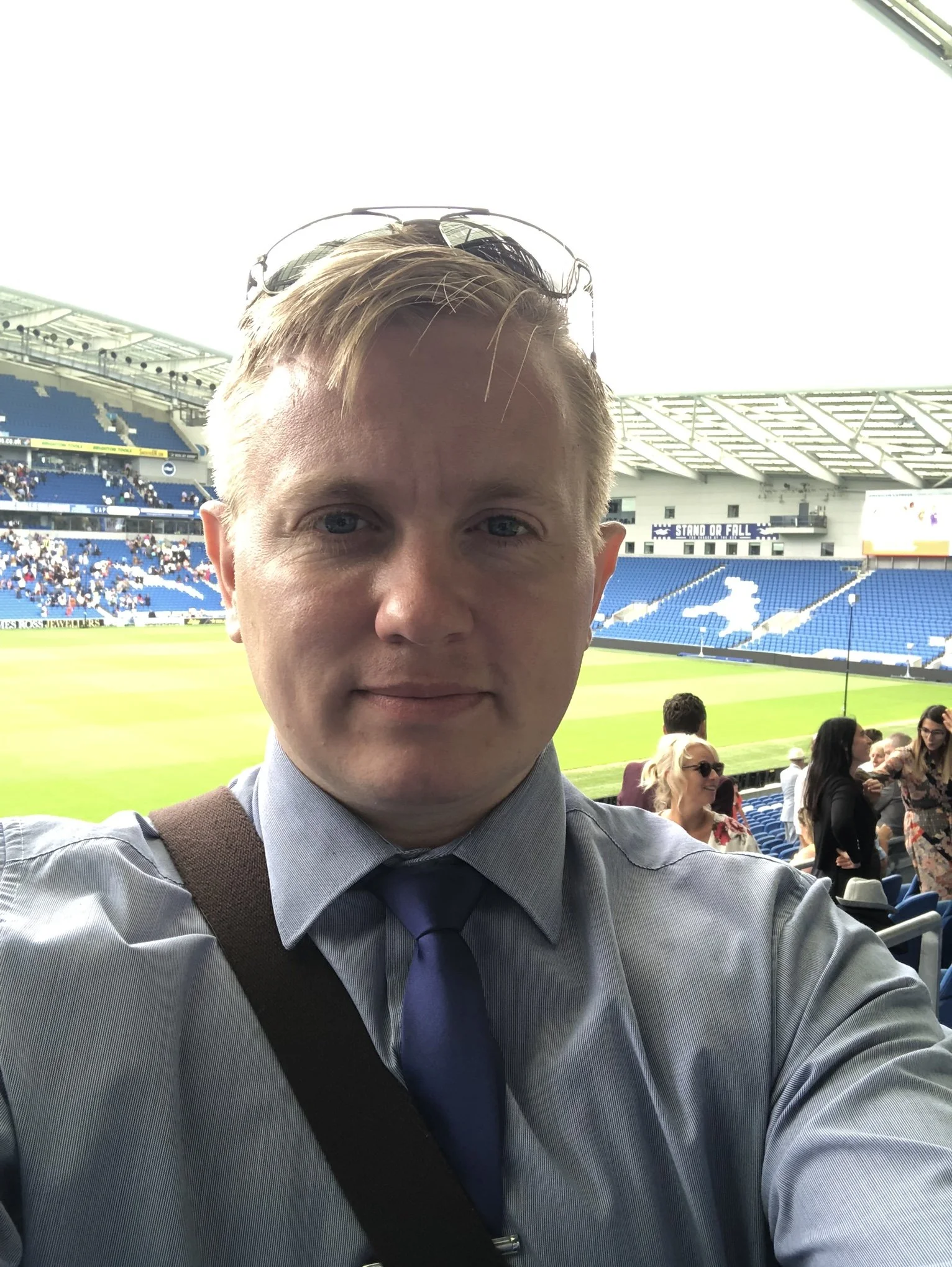A man taking a selfie at a stadium before a sports event, with the field and spectators in the background.