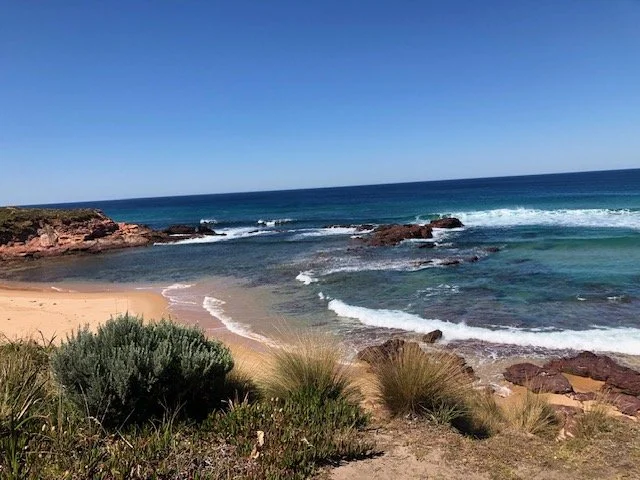 Beach with sandy shore, rocks, and ocean waves under a clear blue sky.