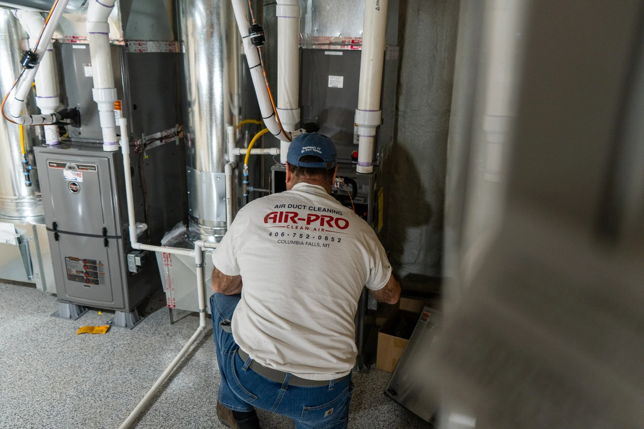A technician working on HVAC equipment in a mechanical room with pipes and electrical components.