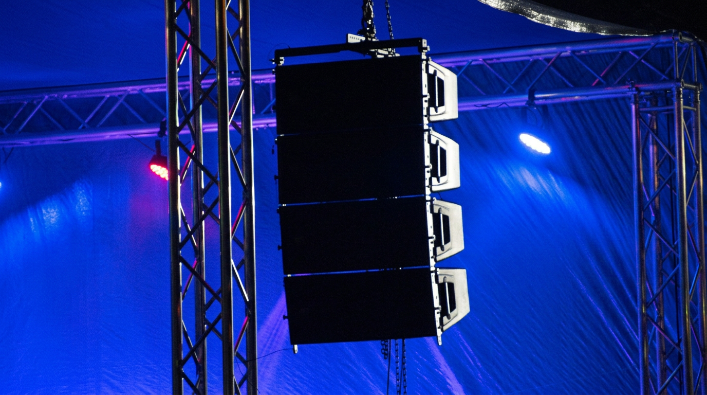 Stage lighting with three black speaker monitors hanging vertically from a metal truss structure under a blue tent canopy.