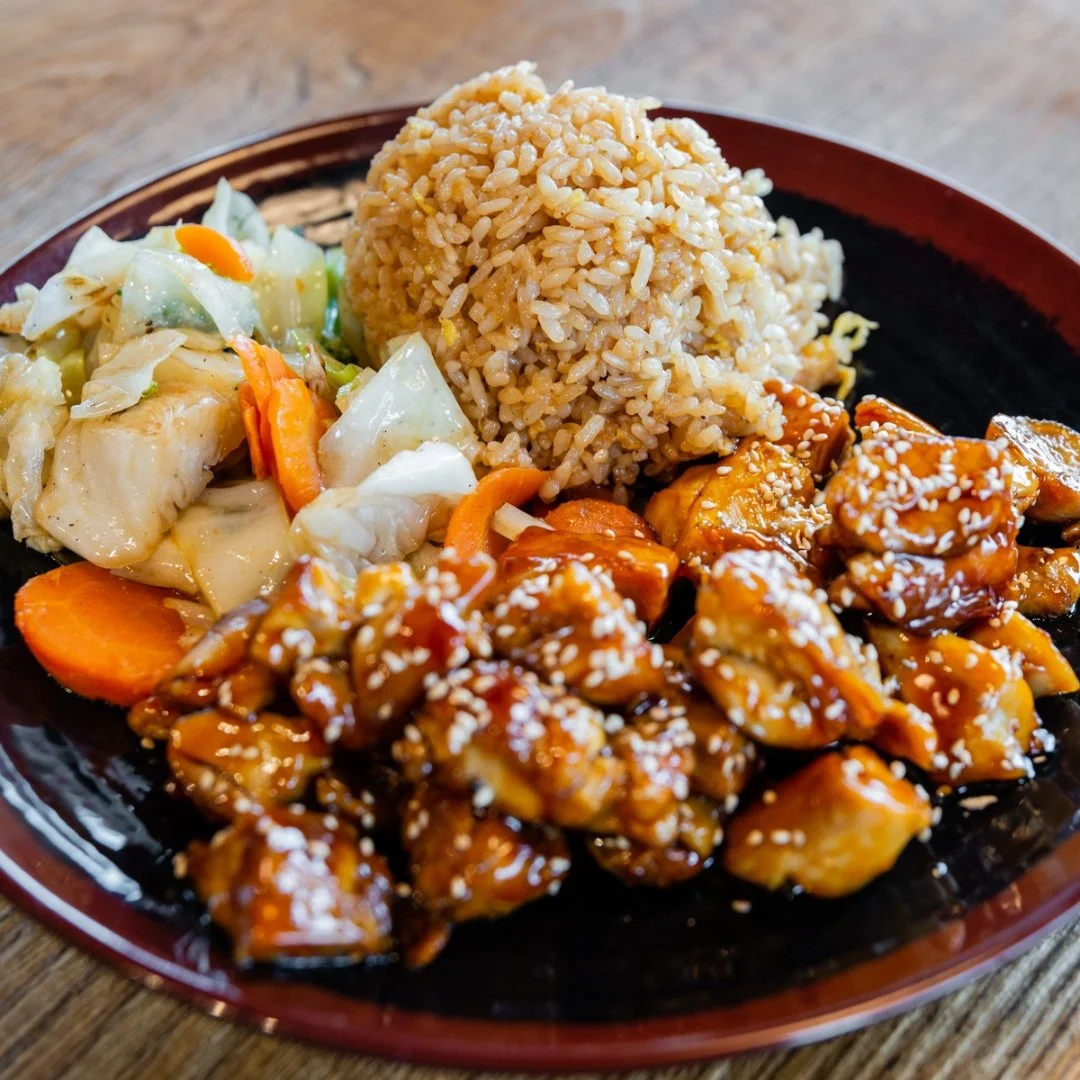 A plate of Asian-inspired food featuring fried rice, orange chicken topped with sesame seeds, and stir-fried vegetables including cabbage and carrots.