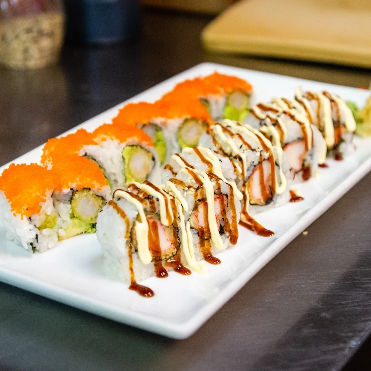 Assorted sushi rolls drizzled with sauces on a white rectangular plate.